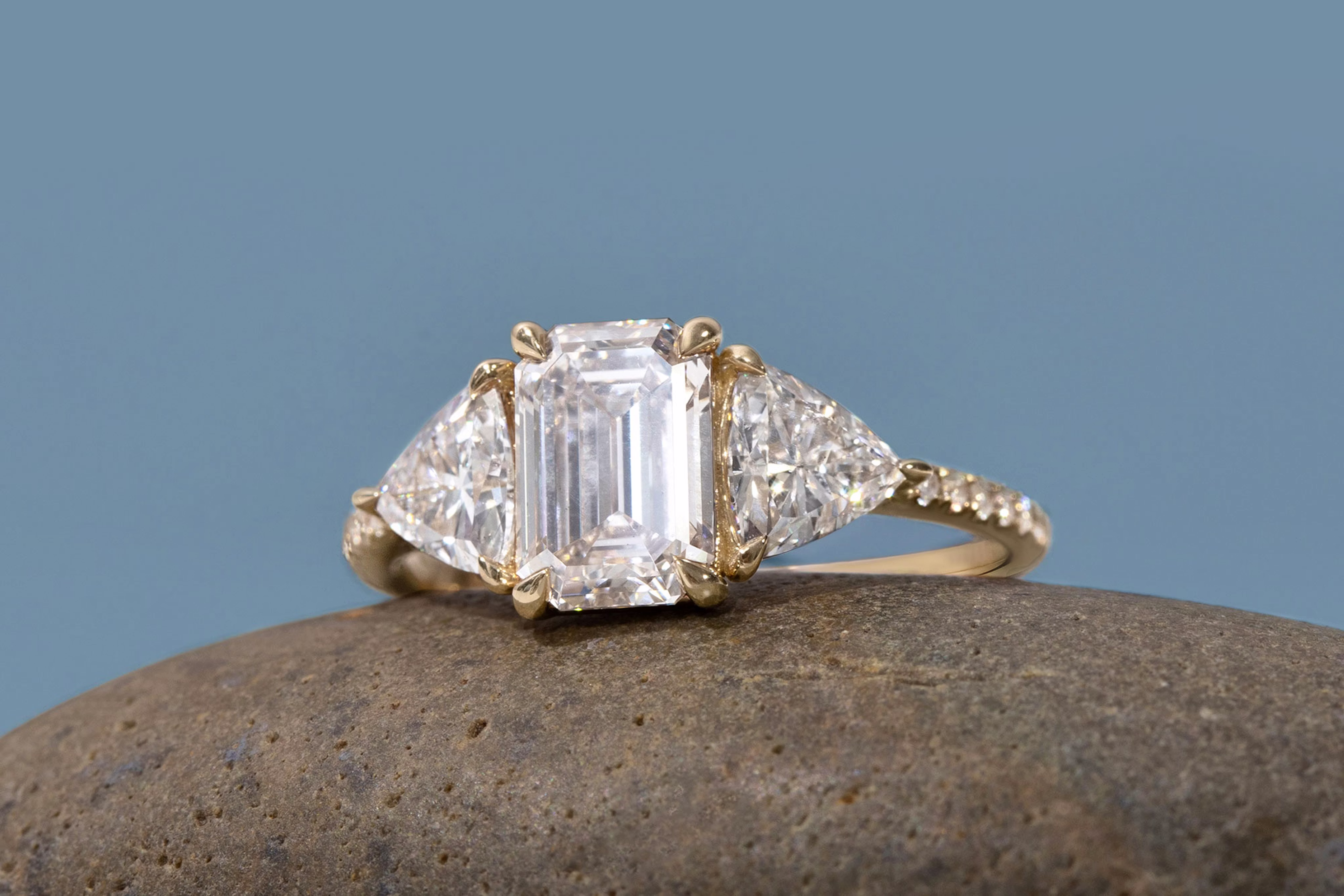 The emerald three stone engagement ring with trillion side stones and yellow gold pave band