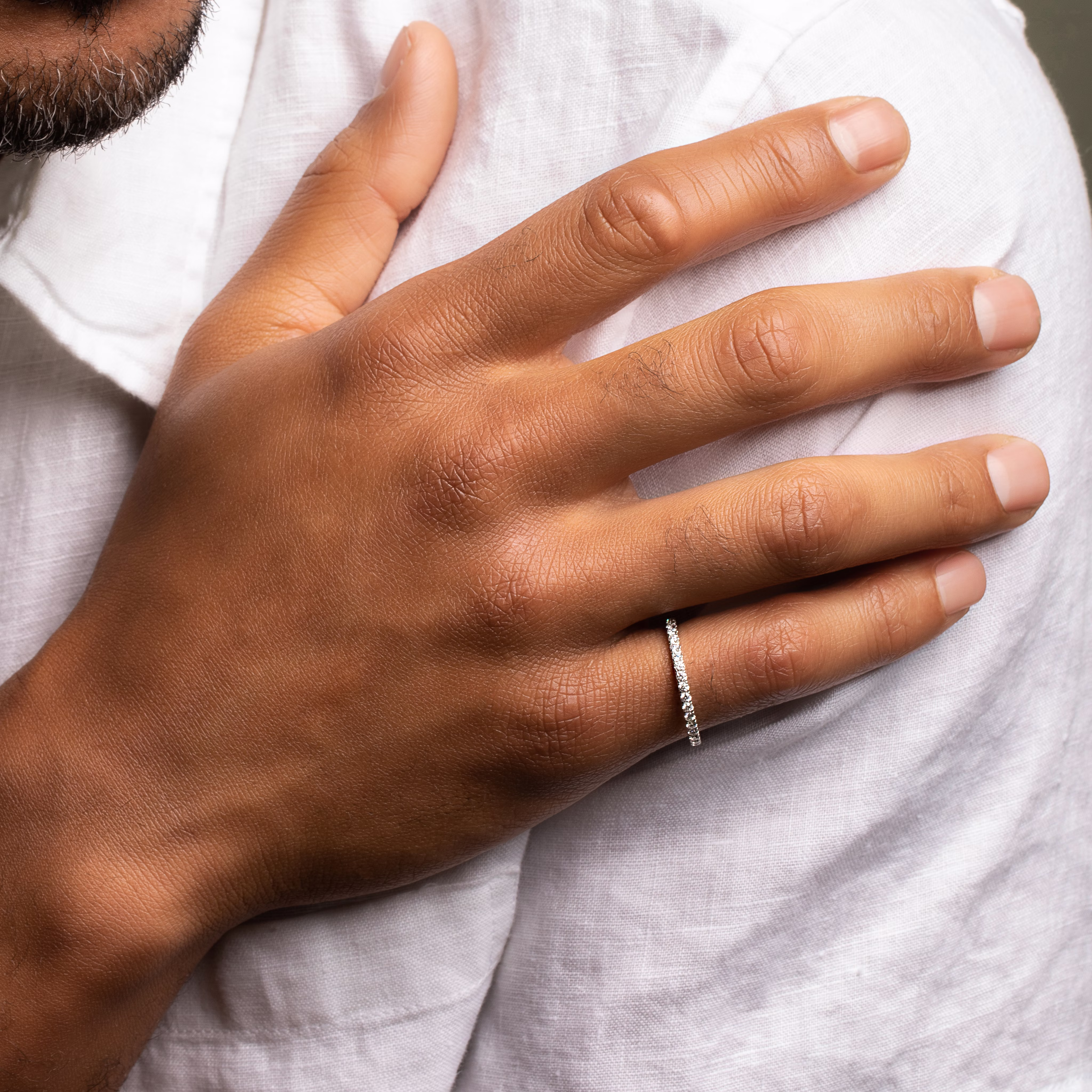 A person's hand wearing a thin, silver-colored eternity band with small inset diamonds.