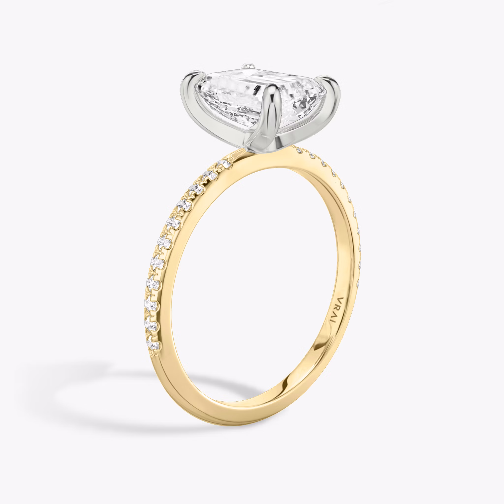 Two-tone engagement ring with emerald-cut diamond, platinum prongs, and pavé yellow gold band, shown in upright side view.