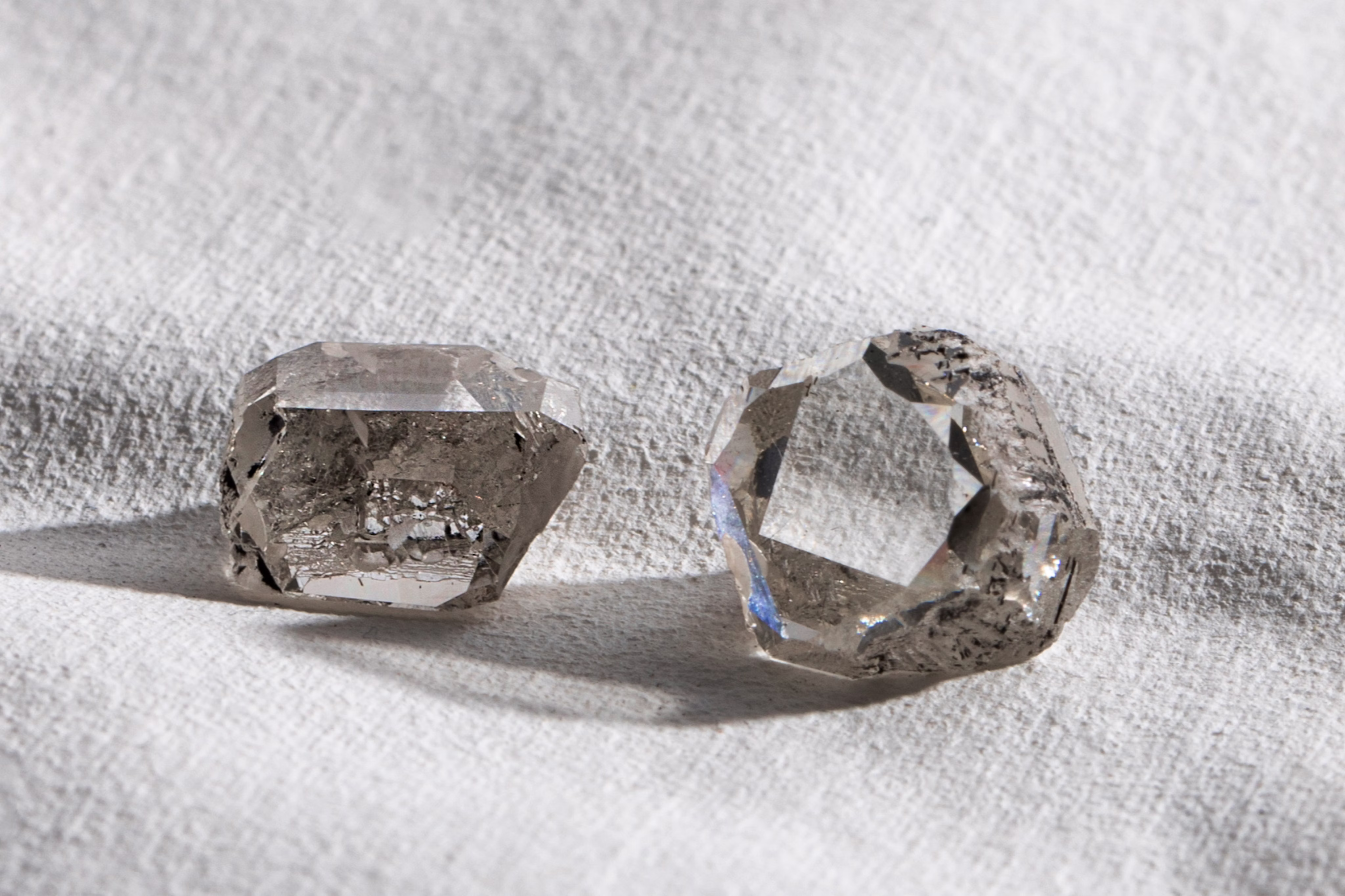Two rough diamonds are lying on a white cloth.
