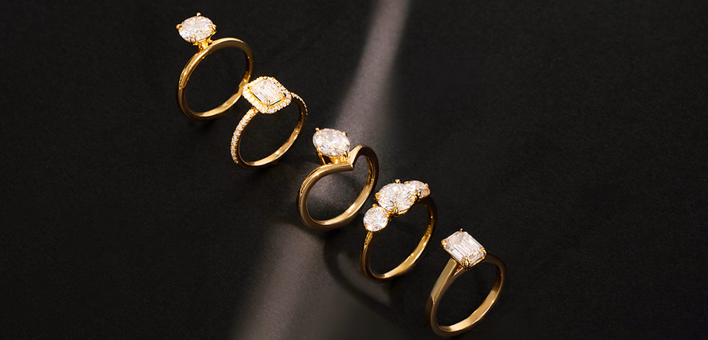 Five engagement rings lined up on a black surface.