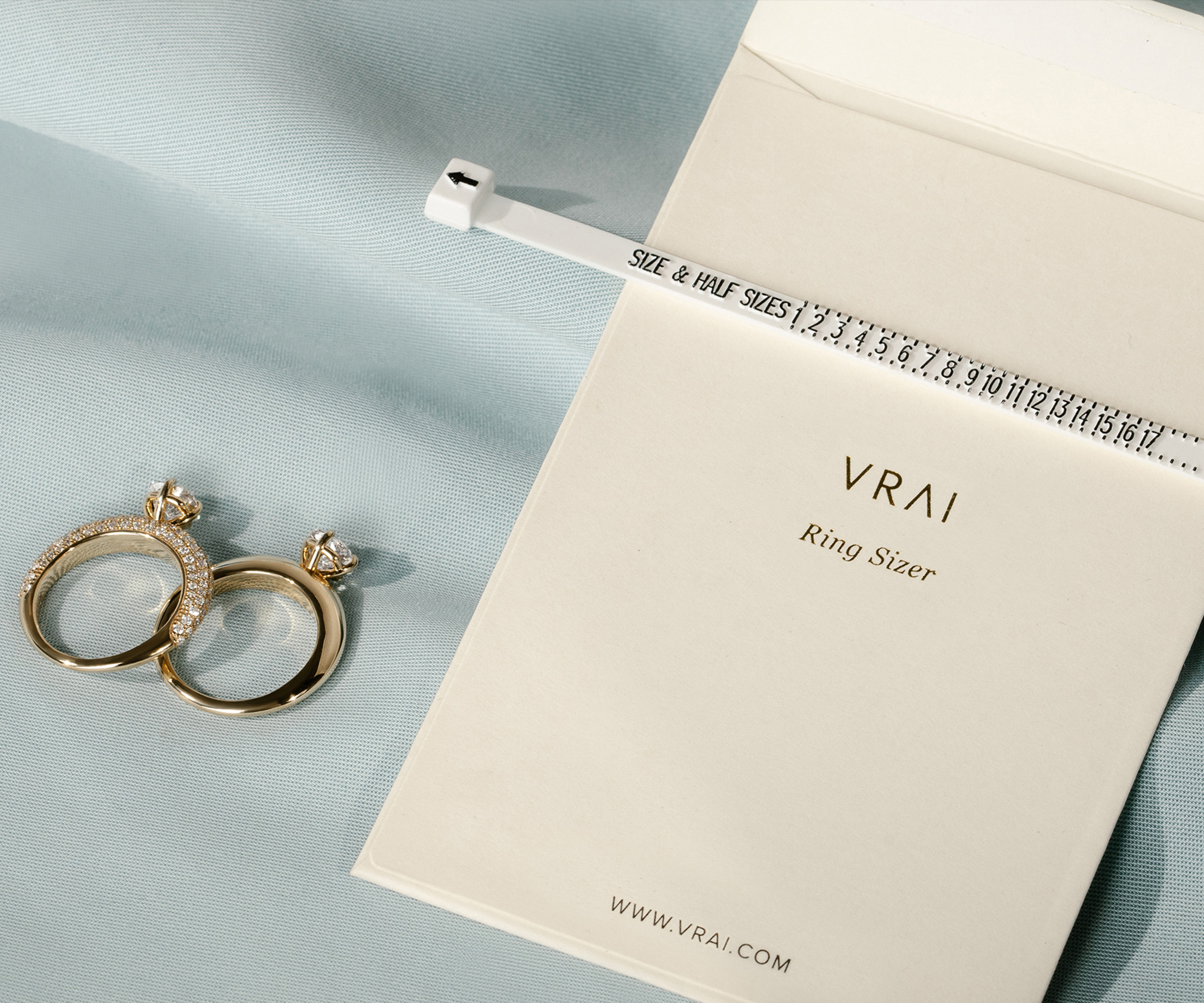 two engagement rings next to a ring sizer and package
