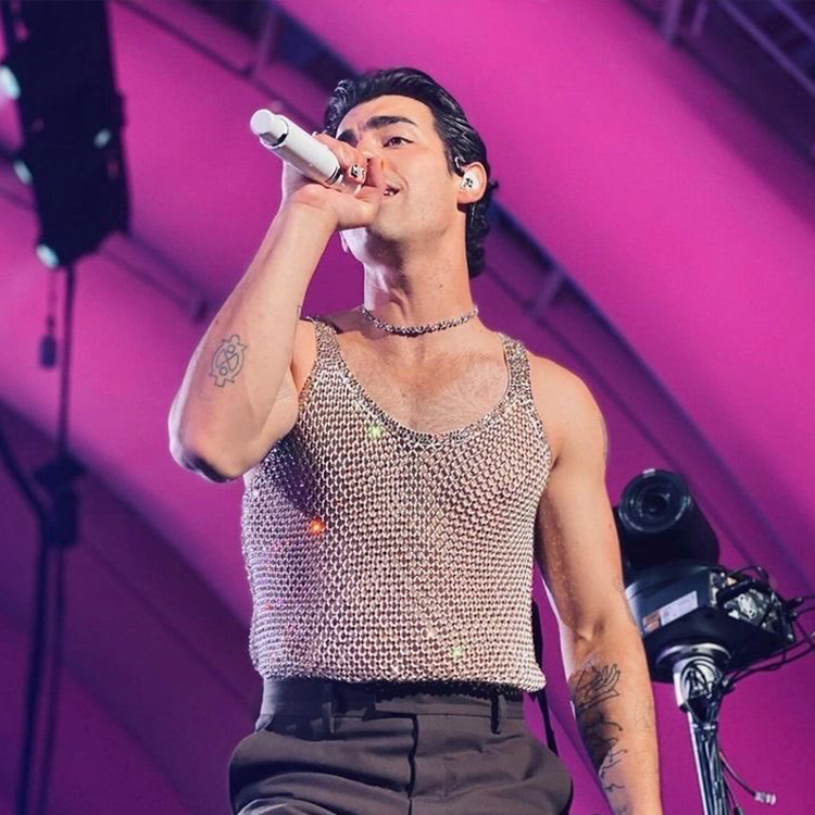 An image of Joe Jonas singing on stage wearing a Round Brilliant Tennis Bracelets, VRAI x RandM Illuminate Choker, and Compass Ring with VRAI created diamonds.