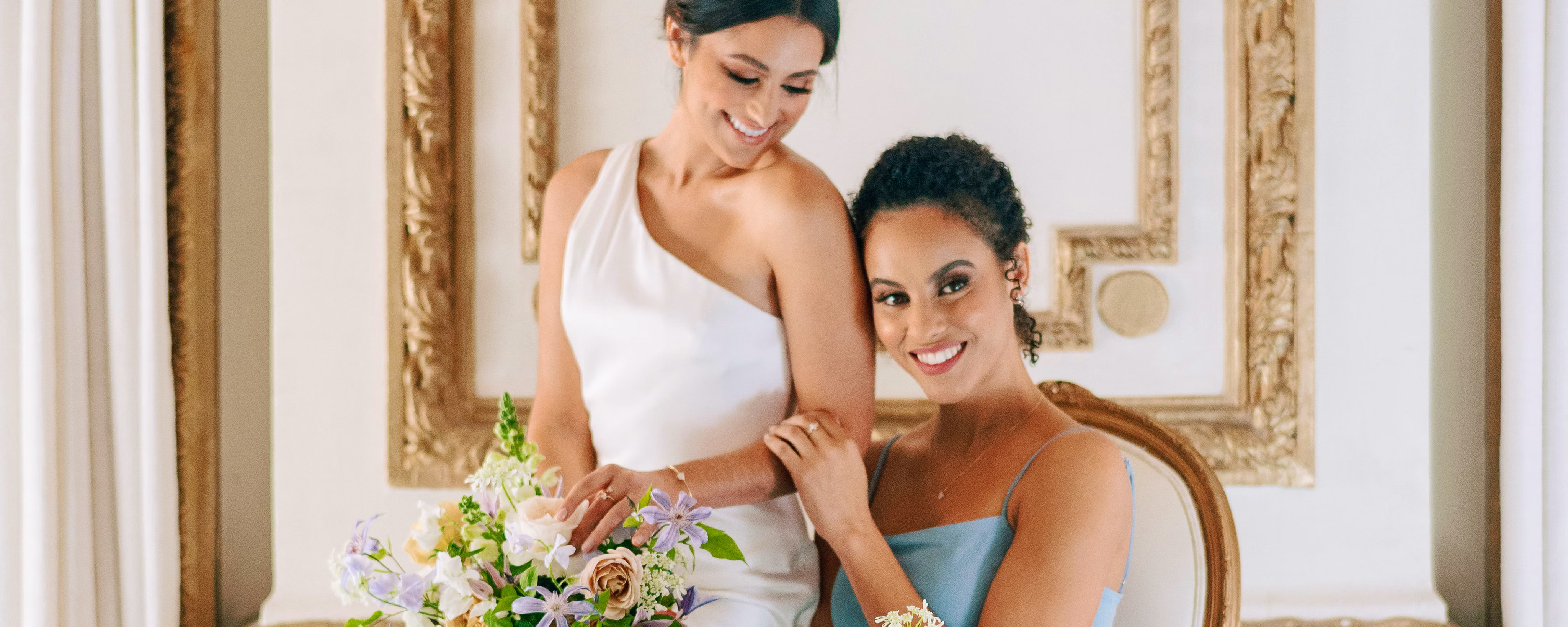An image of a bride holding a flower bouquet and sitting on the lap of a woman wearing a blue dress.
