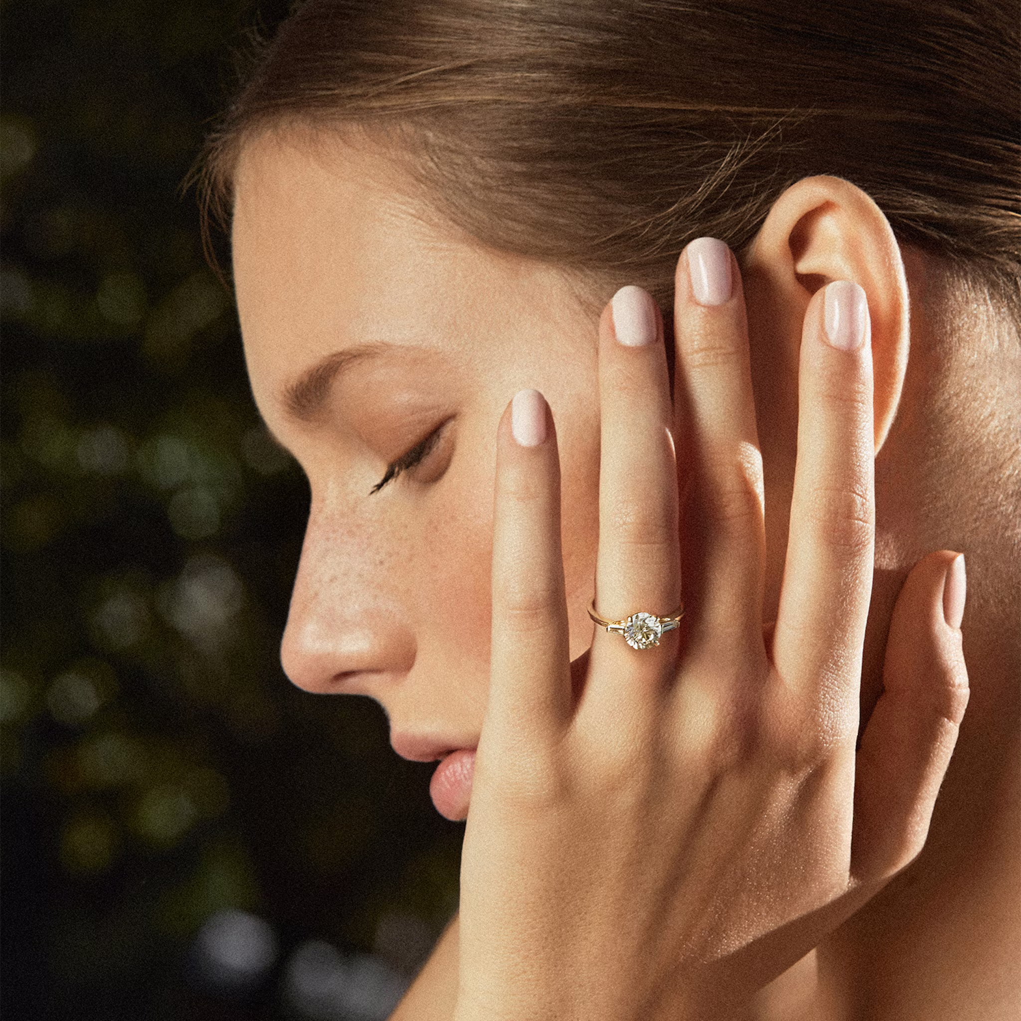 Model wearing a yellow gold three stone engagement ring with round center and tapered baguette side stones