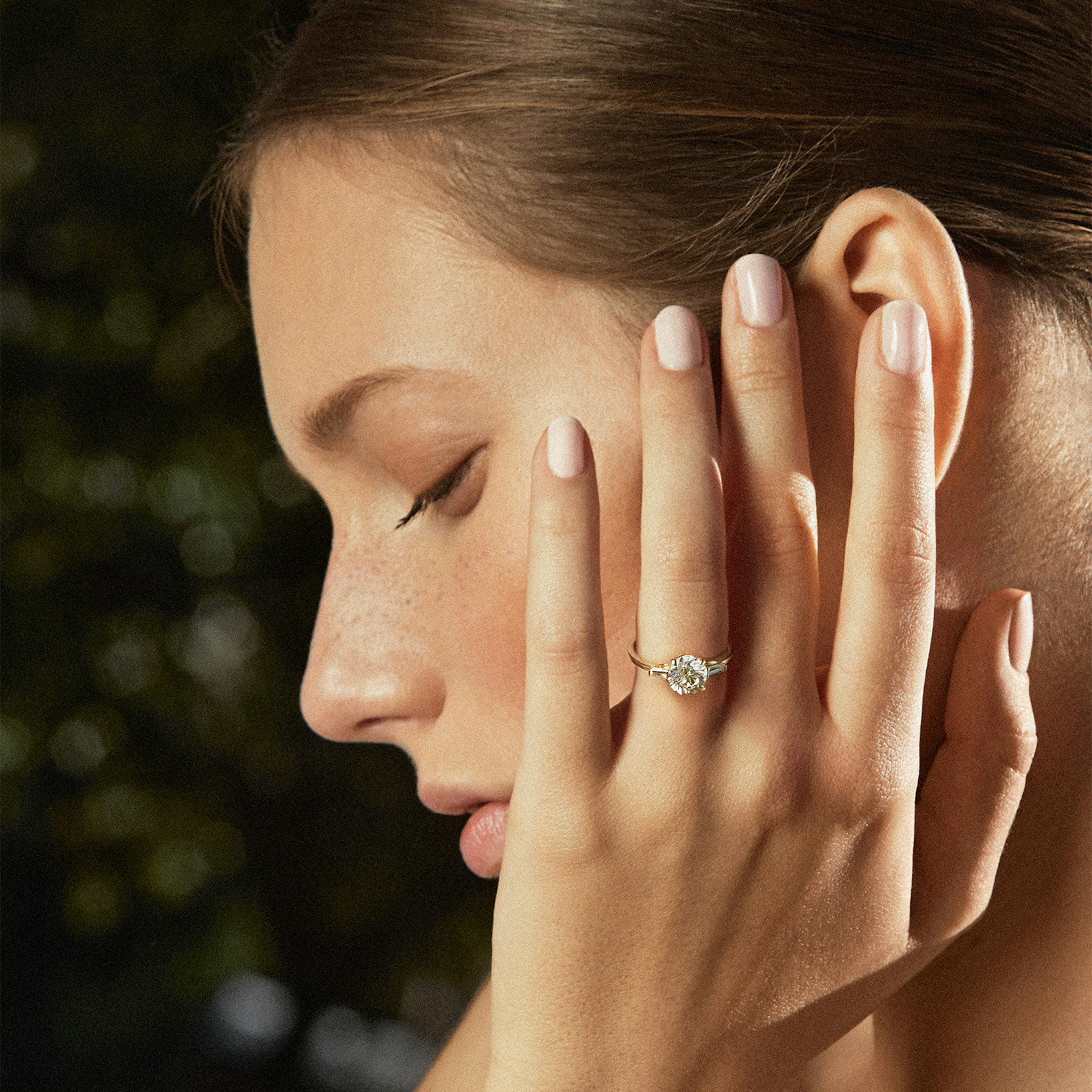 Model wearing a yellow gold three stone engagement ring with round center and tapered baguette side stones