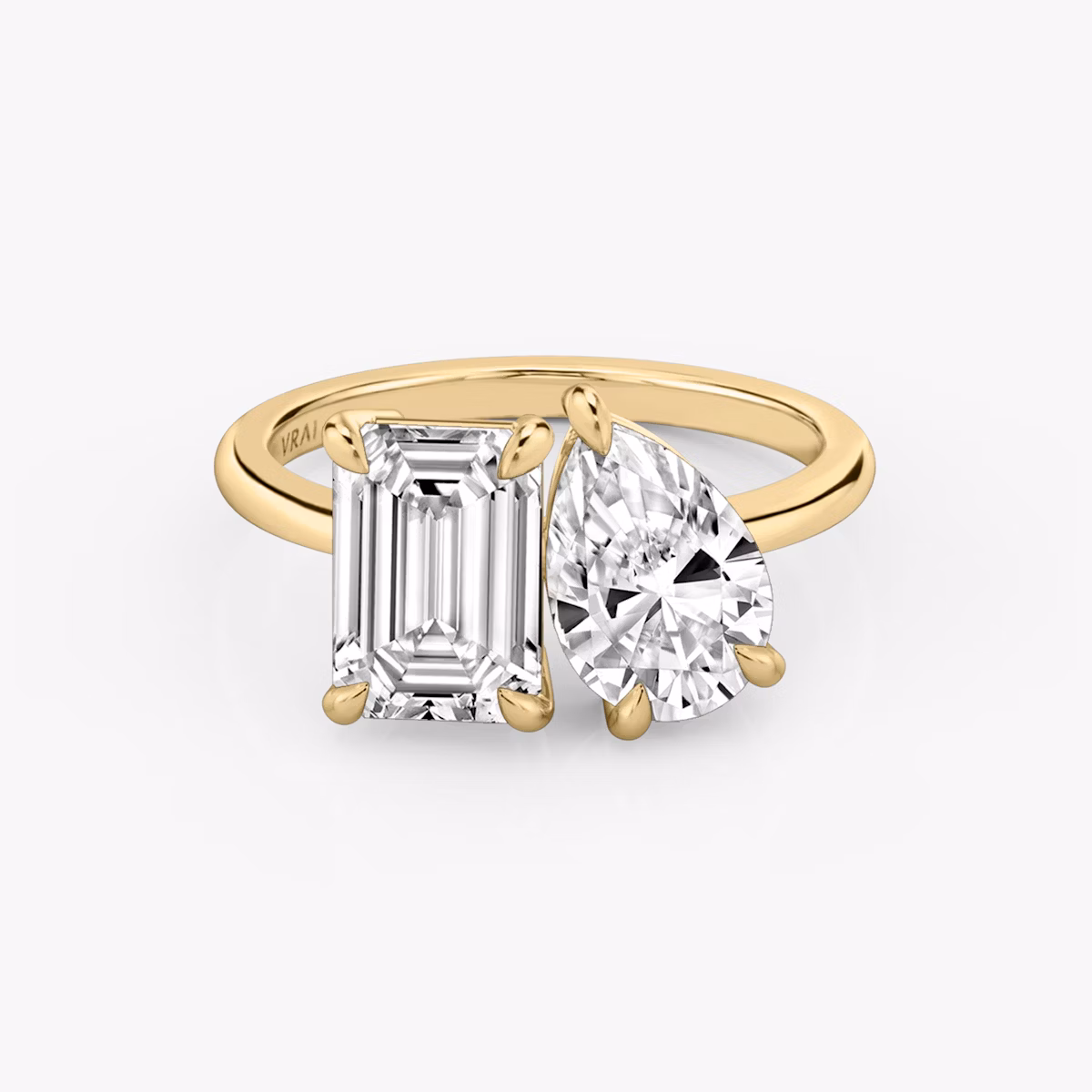 Yellow gold Toi et Moi ring with one pear-cut and one emerald-cut center diamond, set on a plain band, shown on white background.