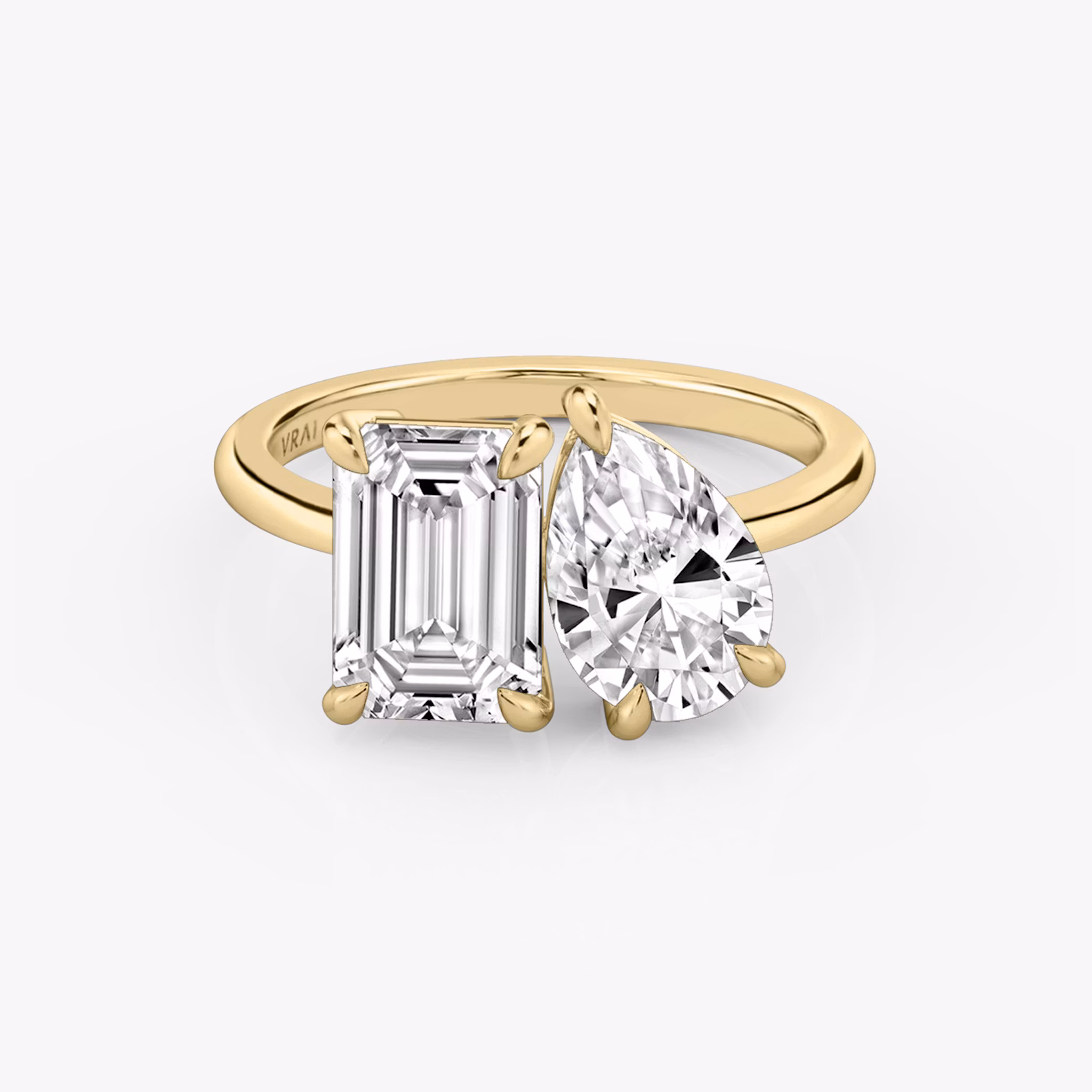 Anillo Toi et Moi con diamantes talla esmeralda y pera en montura de oro amarillo, sobre fondo blanco.