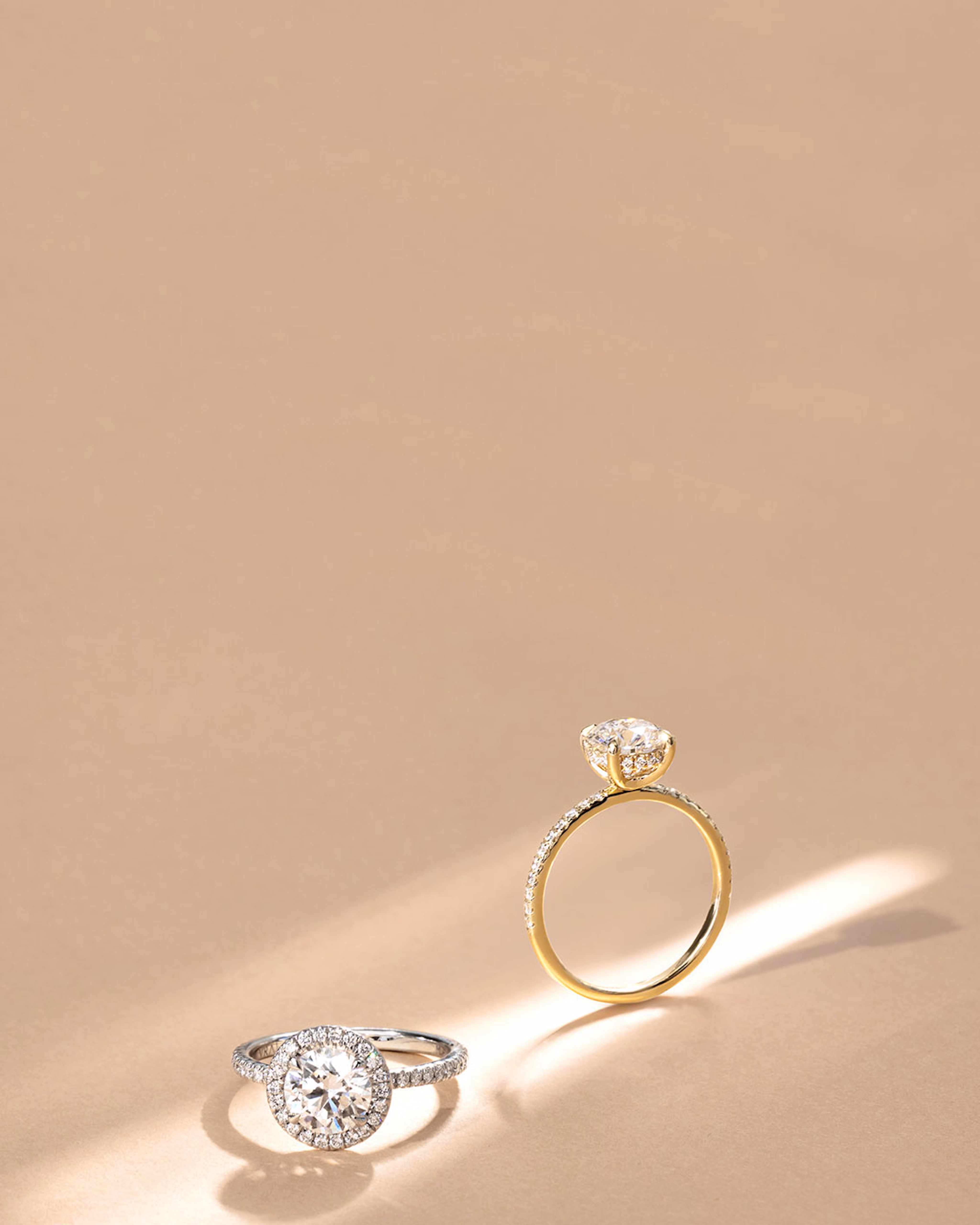 Zwei VRAI-Verlobungsringe auf hellbraunem Hintergrund.