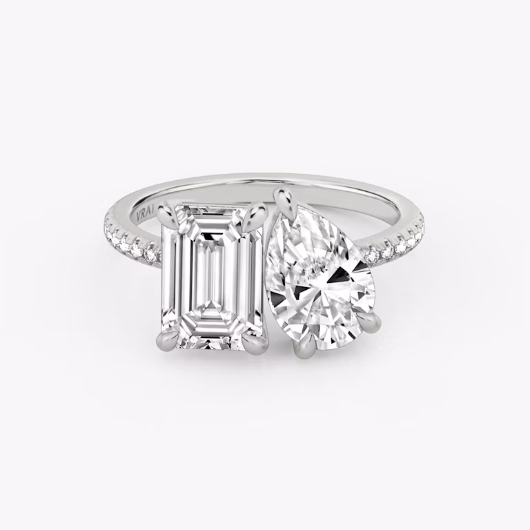 Toi et Moi ring with emerald and pear-cut diamonds on a pavé white gold band, designed for a modern yet elegant engagement look.