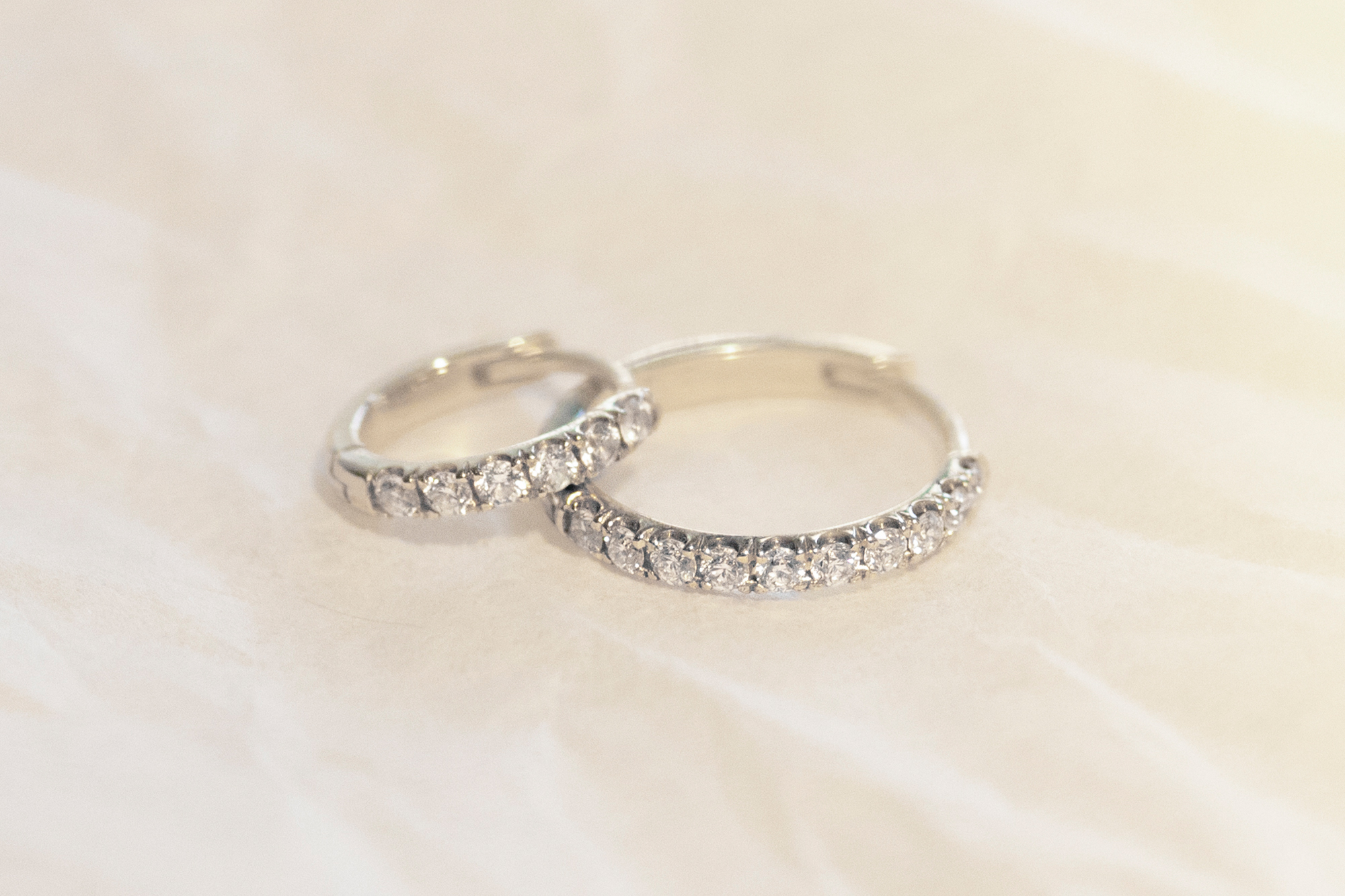 Two silver Pavé bands are resting on one another, on a textured, white surface.