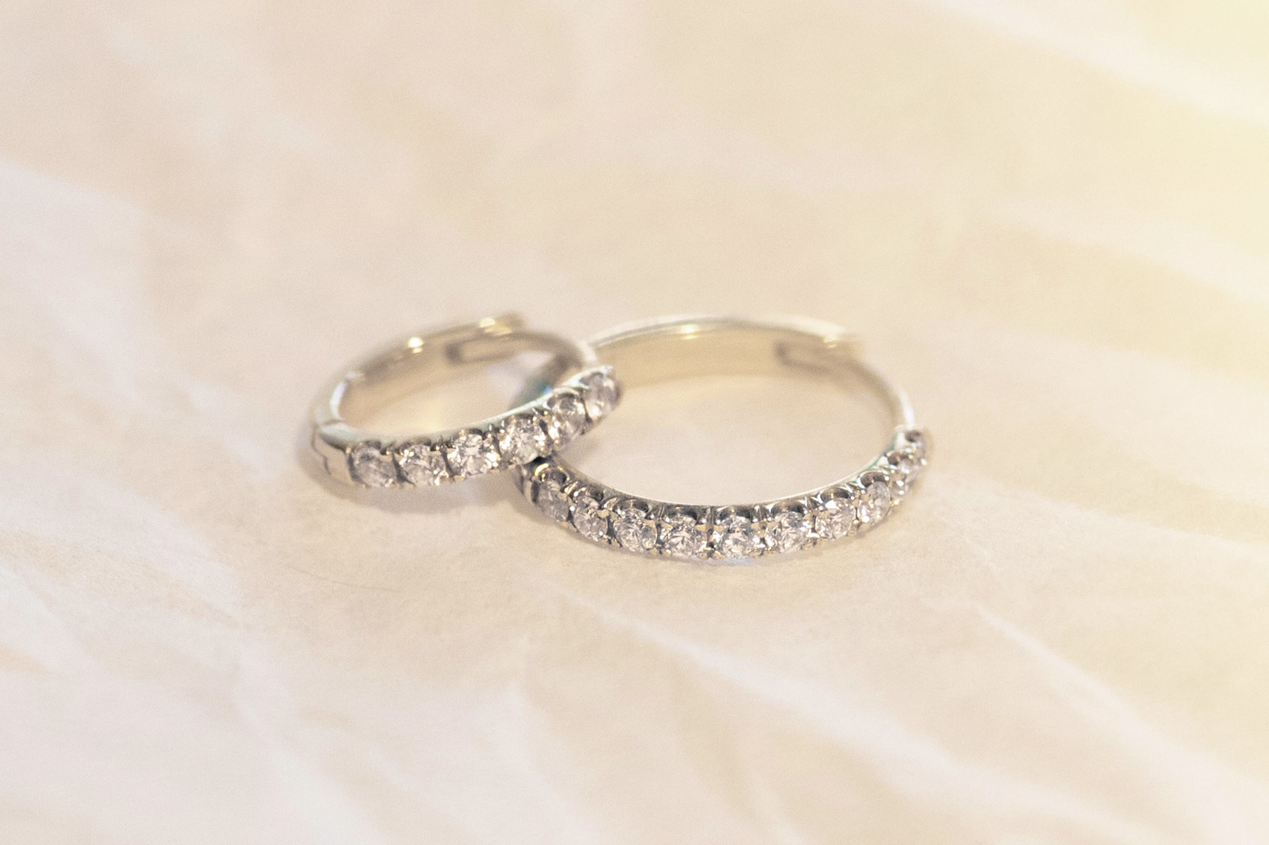 Two silver Pavé bands are resting on one another, on a textured, white surface.