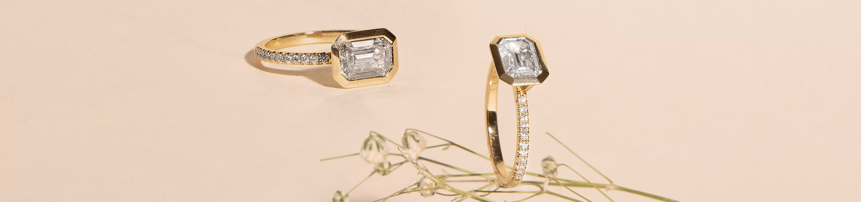 Two emerald-cut engagement rings, one of which is sitting on Baby's Breath.