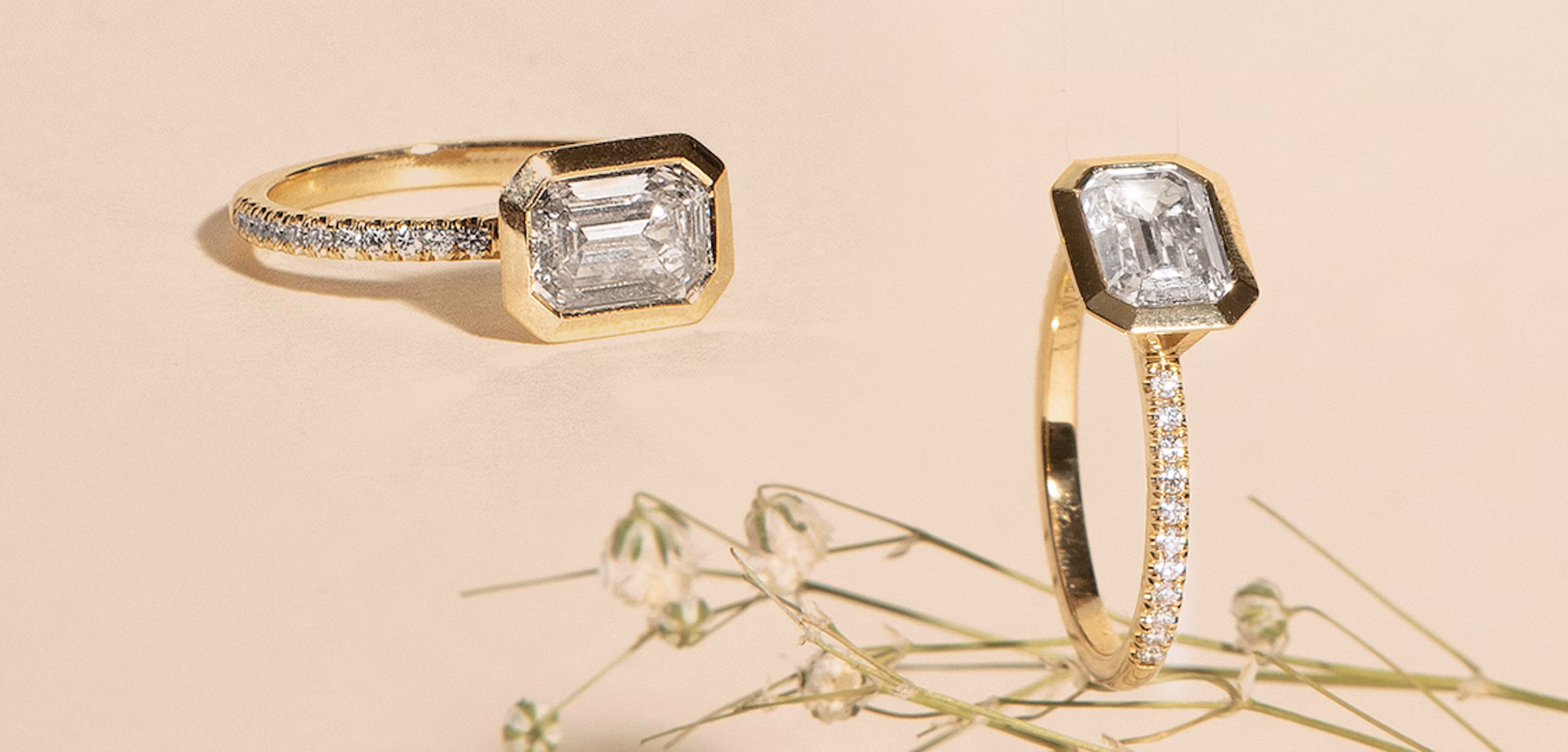 Two emerald-cut engagement rings, one of which is sitting on Baby's Breath.