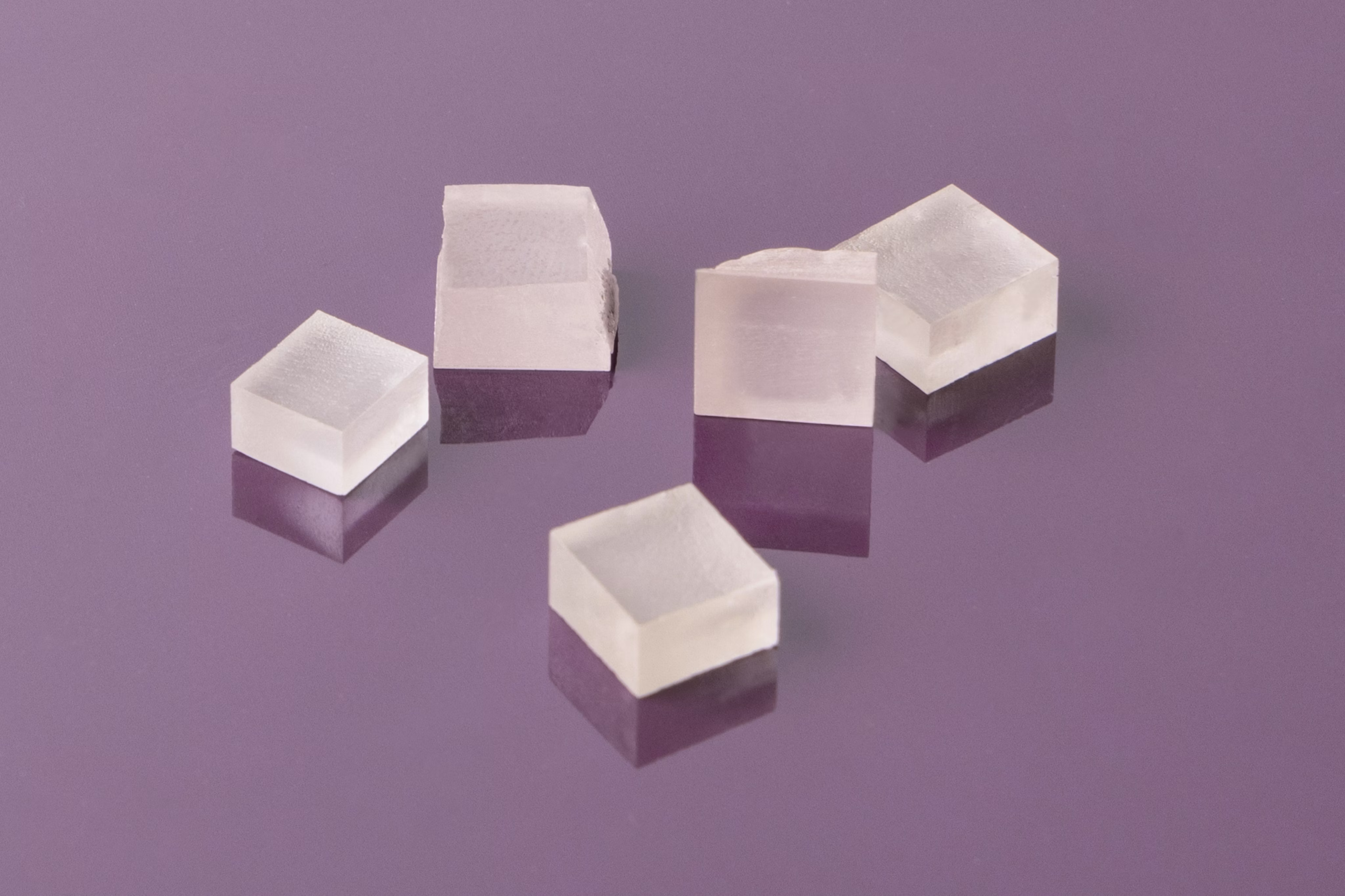 Five loose-cut diamonds on purple surface, showcasing sparkle, clarity, and precision cuts.