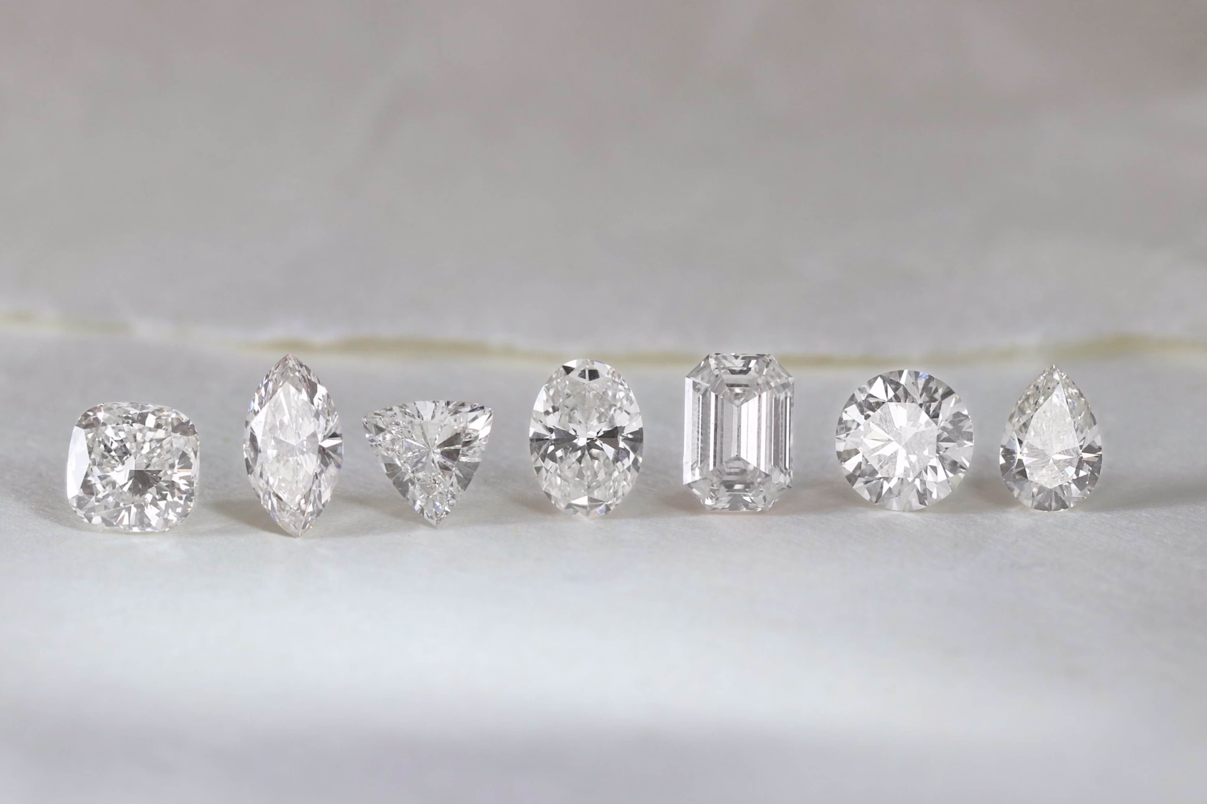 Several different cuts of lab-grown diamonds are lined up on a white surface.