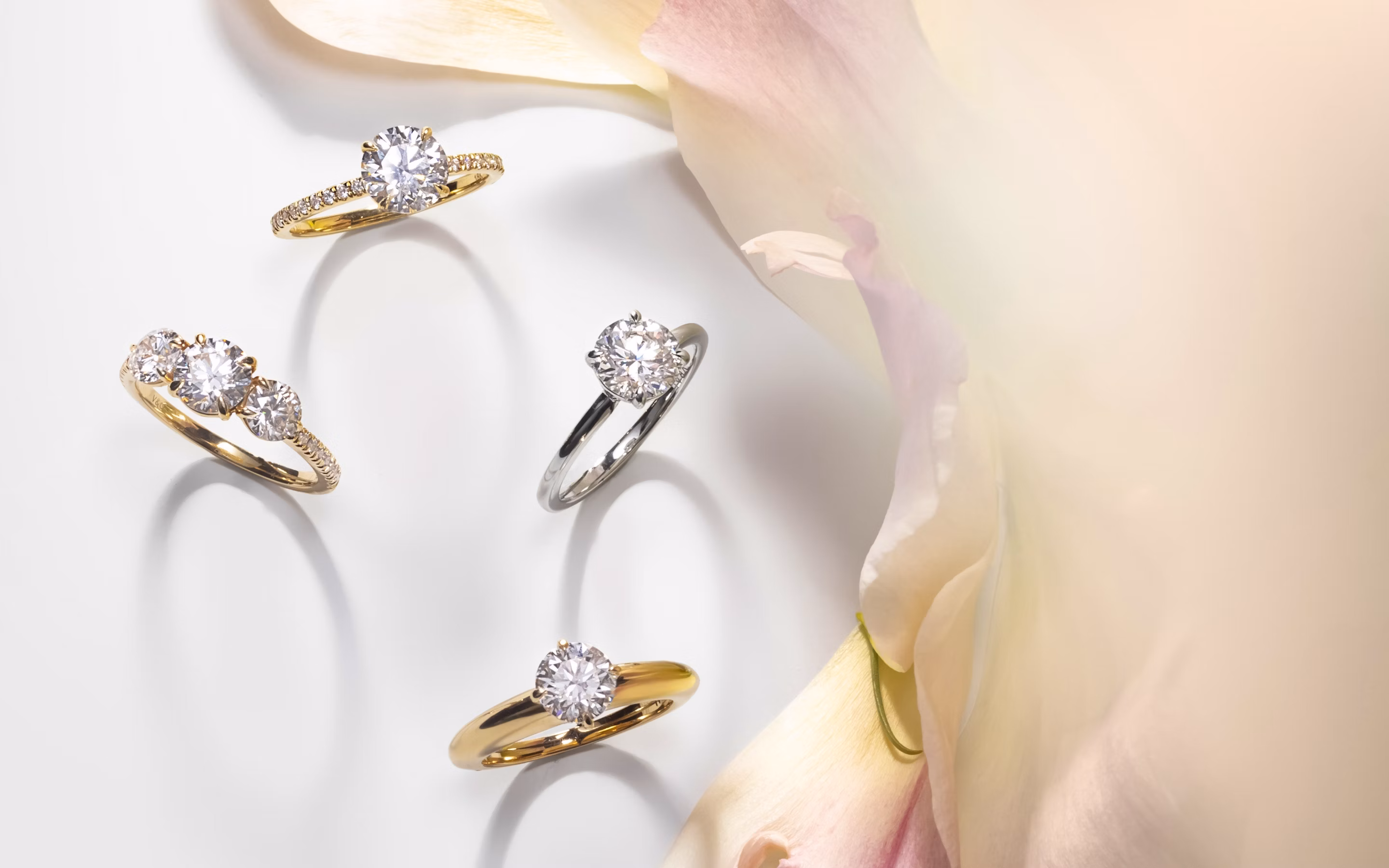 four engagement rings with round brilliant diamonds with different settings next an image of flowers