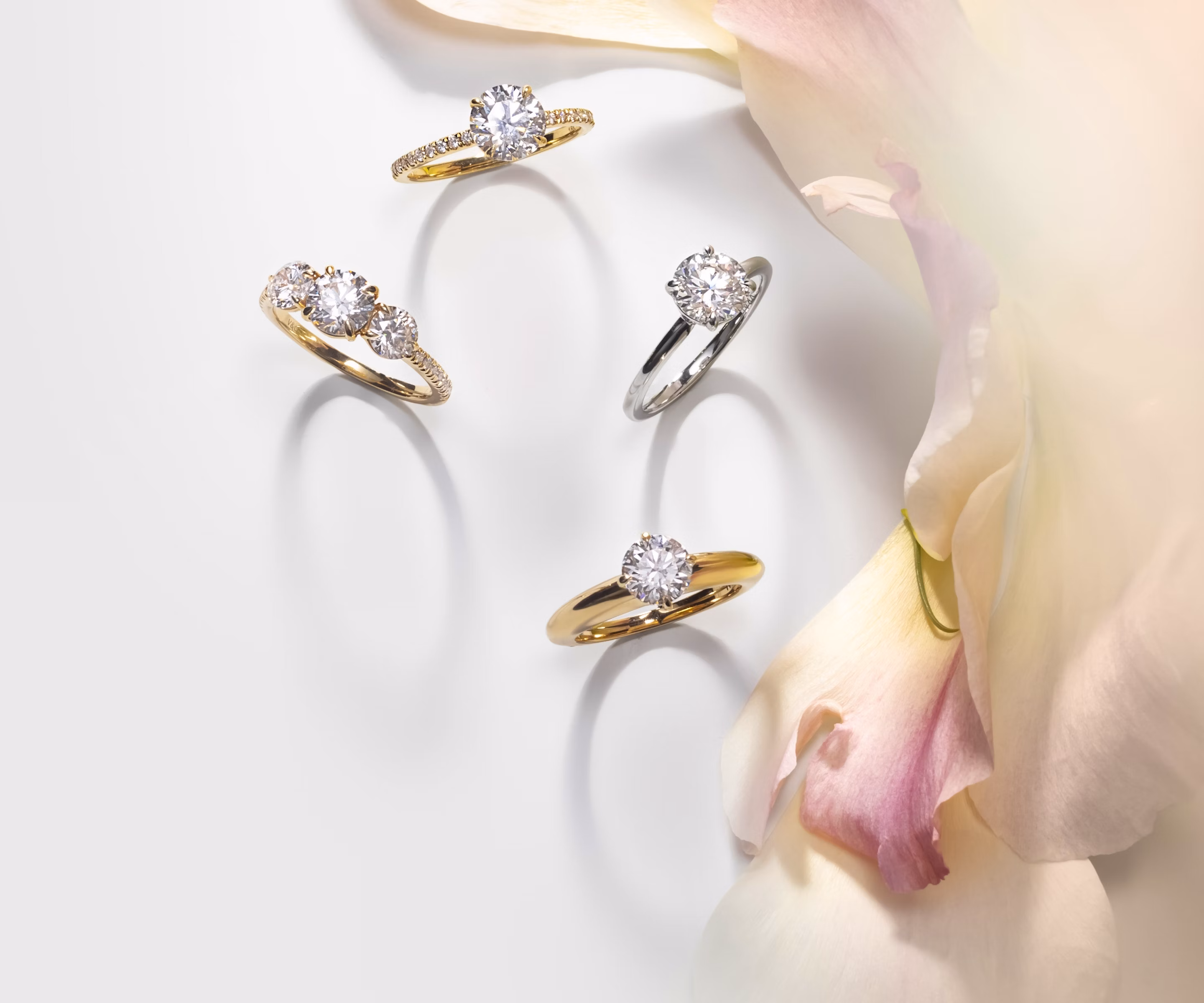 four engagement rings with round brilliant diamonds with different settings next an image of flowers