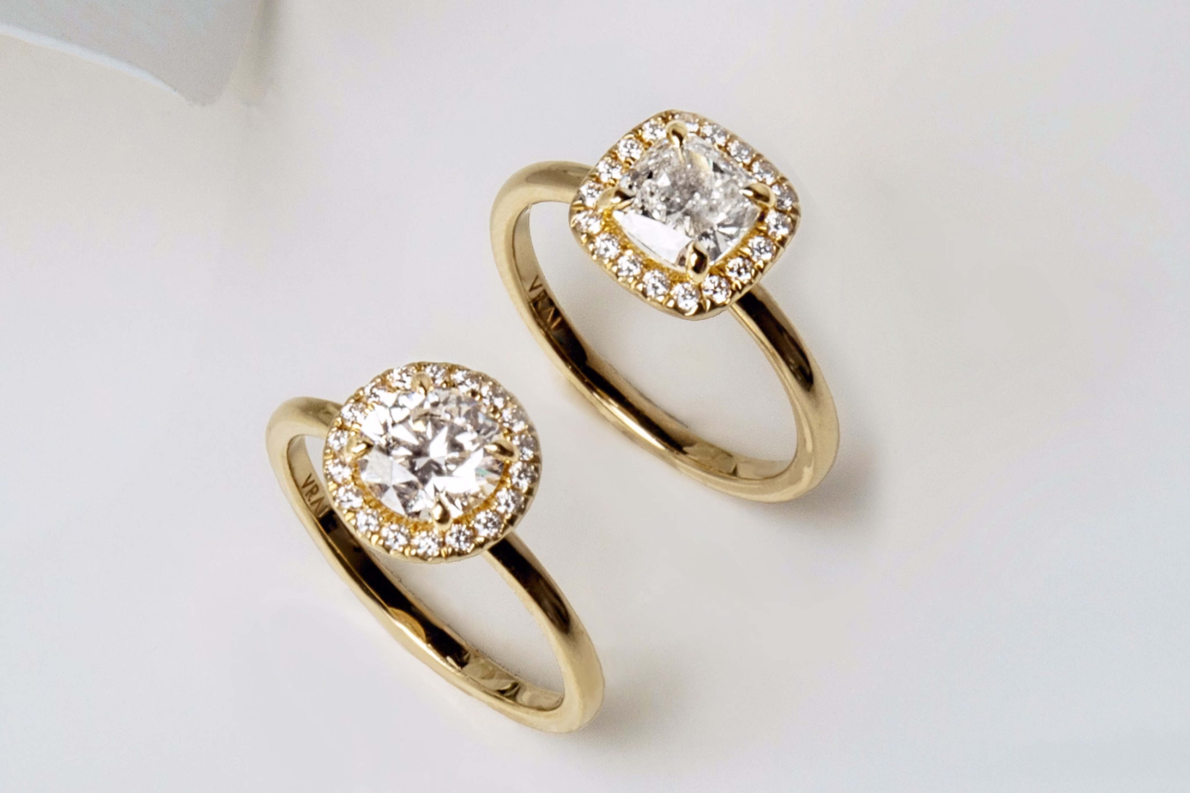 Yellow Gold Round Engagement Ring and a Yellow Gold Cushion Engagement Ring on a white surface.