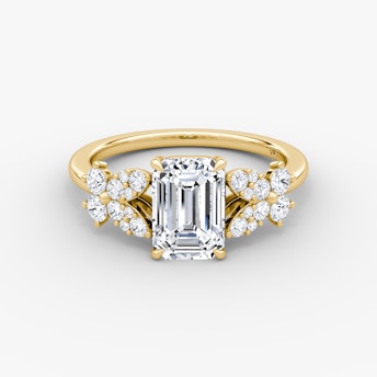 Front view of a signature floral emerald engagement ring in plain yellow gold on a white background.