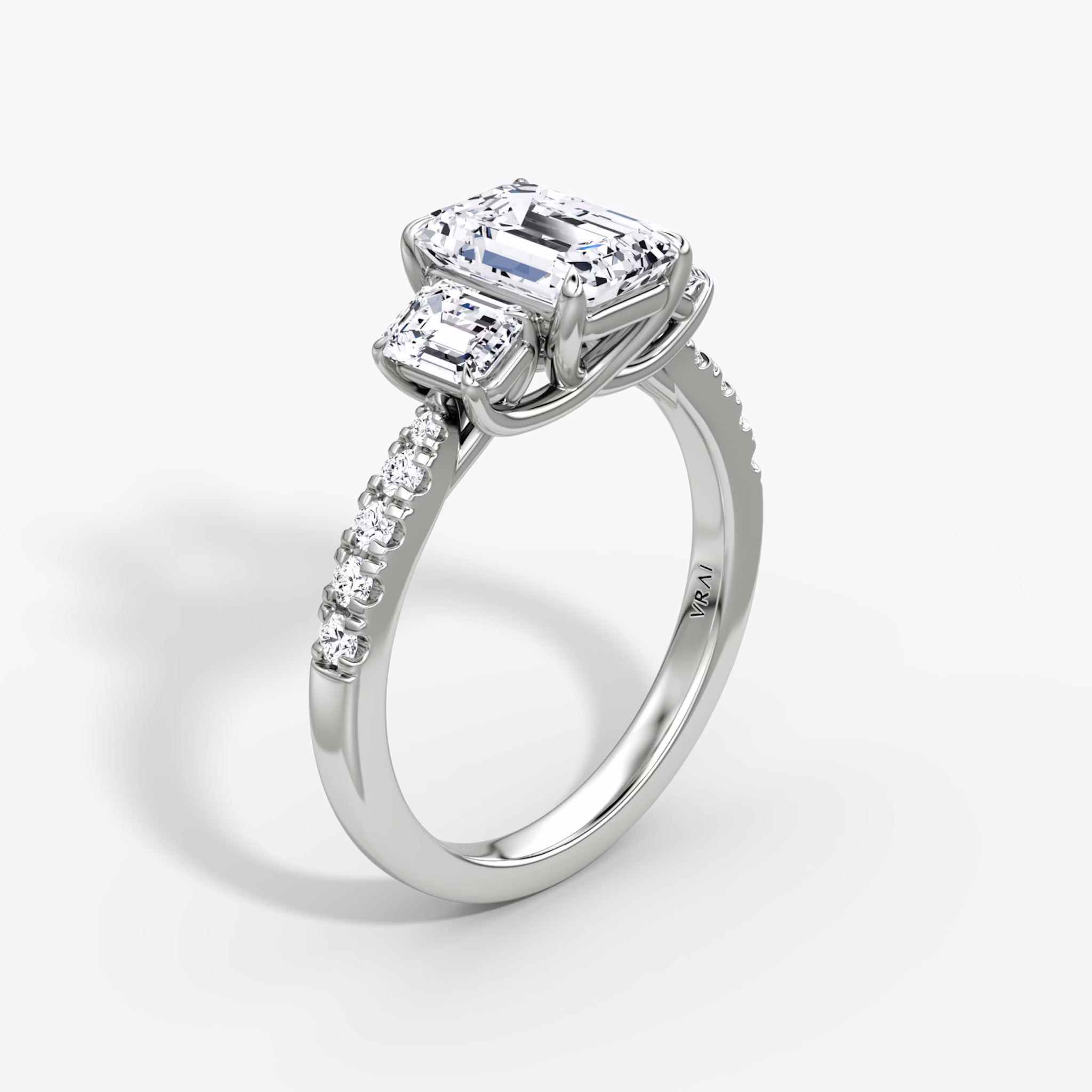 Emerald-cut three-stone diamond ring with pavé band in platinum, VRAI Trellis setting.