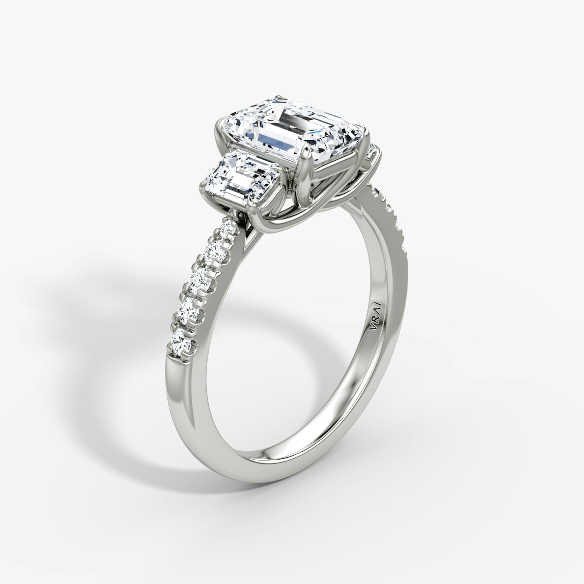 Emerald-cut three-stone diamond ring with pavé band in platinum, VRAI Trellis setting.