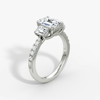 Emerald-cut three-stone diamond ring with pavé band in platinum, VRAI Trellis setting.