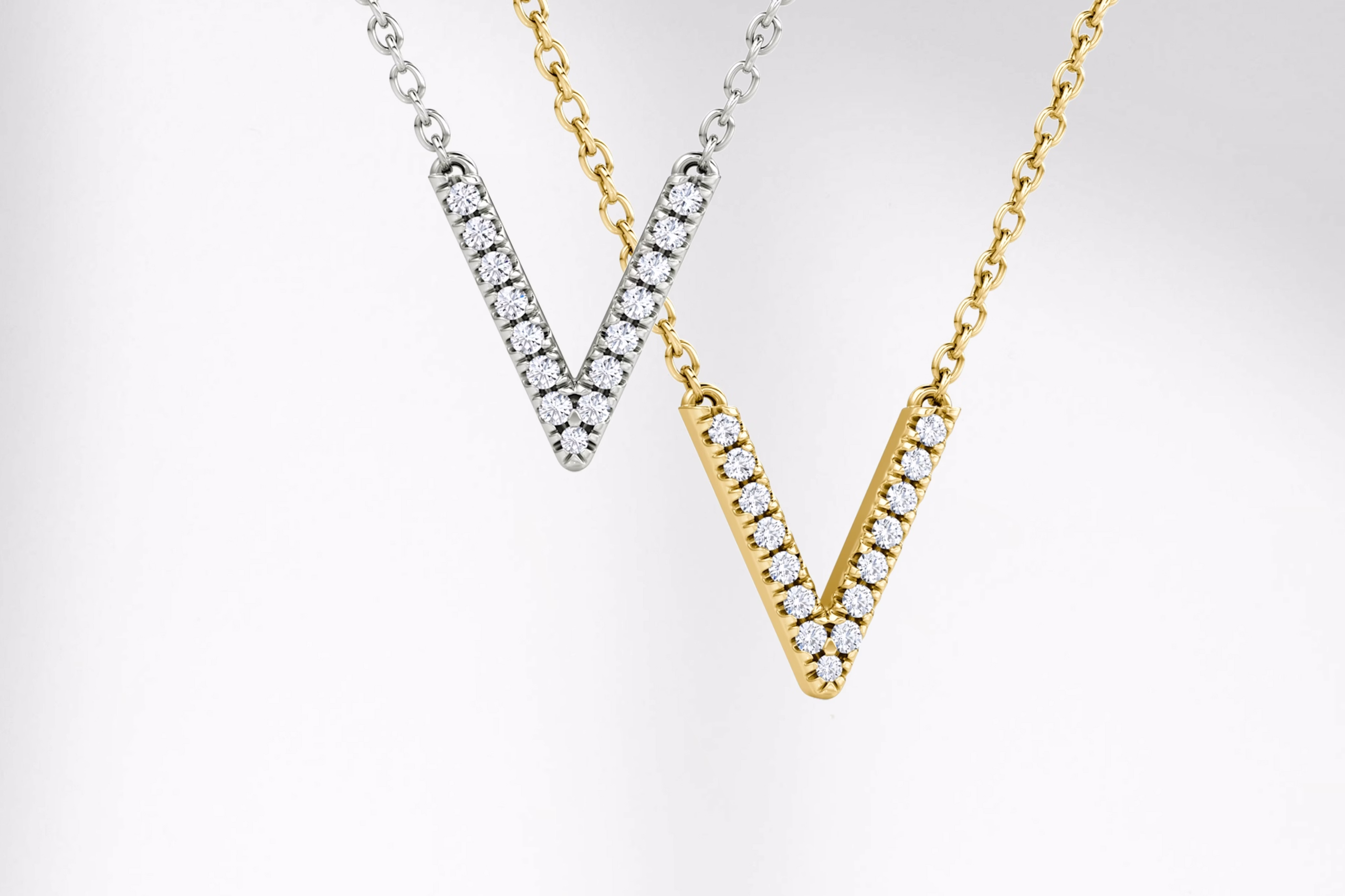 Two V-shaped diamond pendant necklaces in white gold and yellow gold, suspended on delicate chains against a white background.