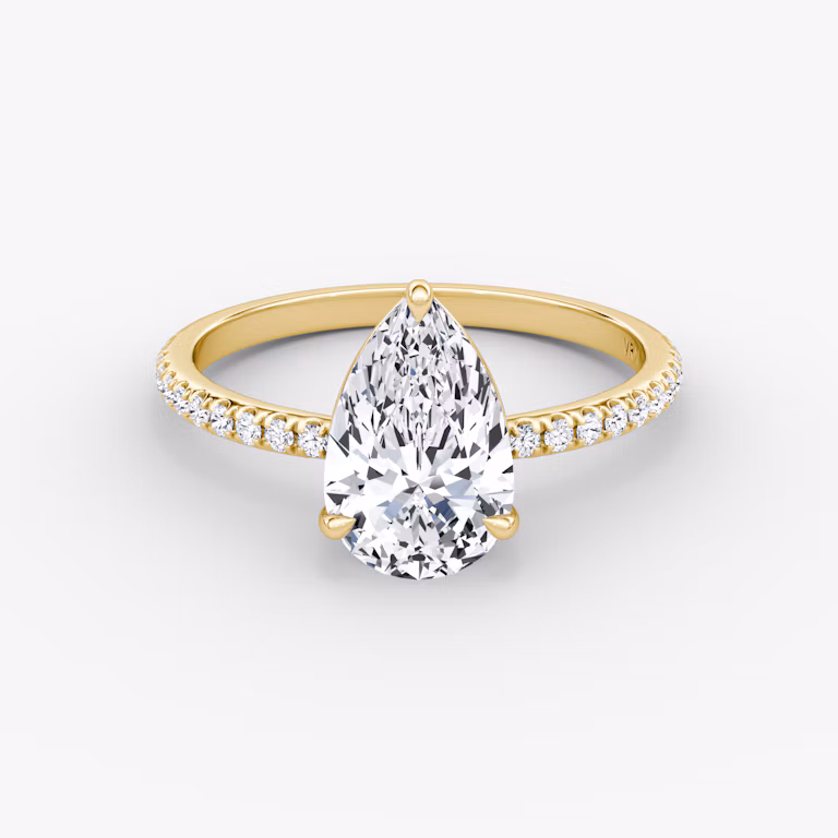 Yellow gold pavé ring with pear-cut center diamond in signature prong setting, shown on white background.