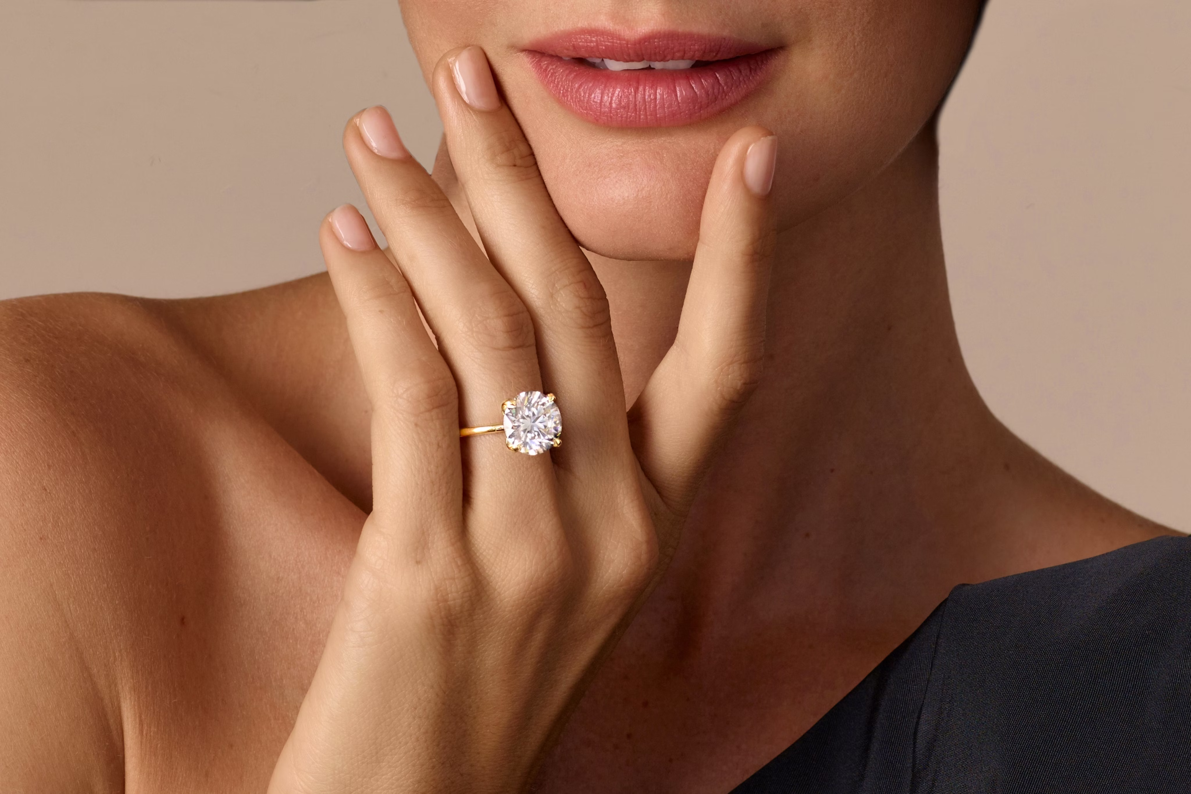 A woman is resting her hand on her chin, with a VRAI created diamond ring on her ring finger.