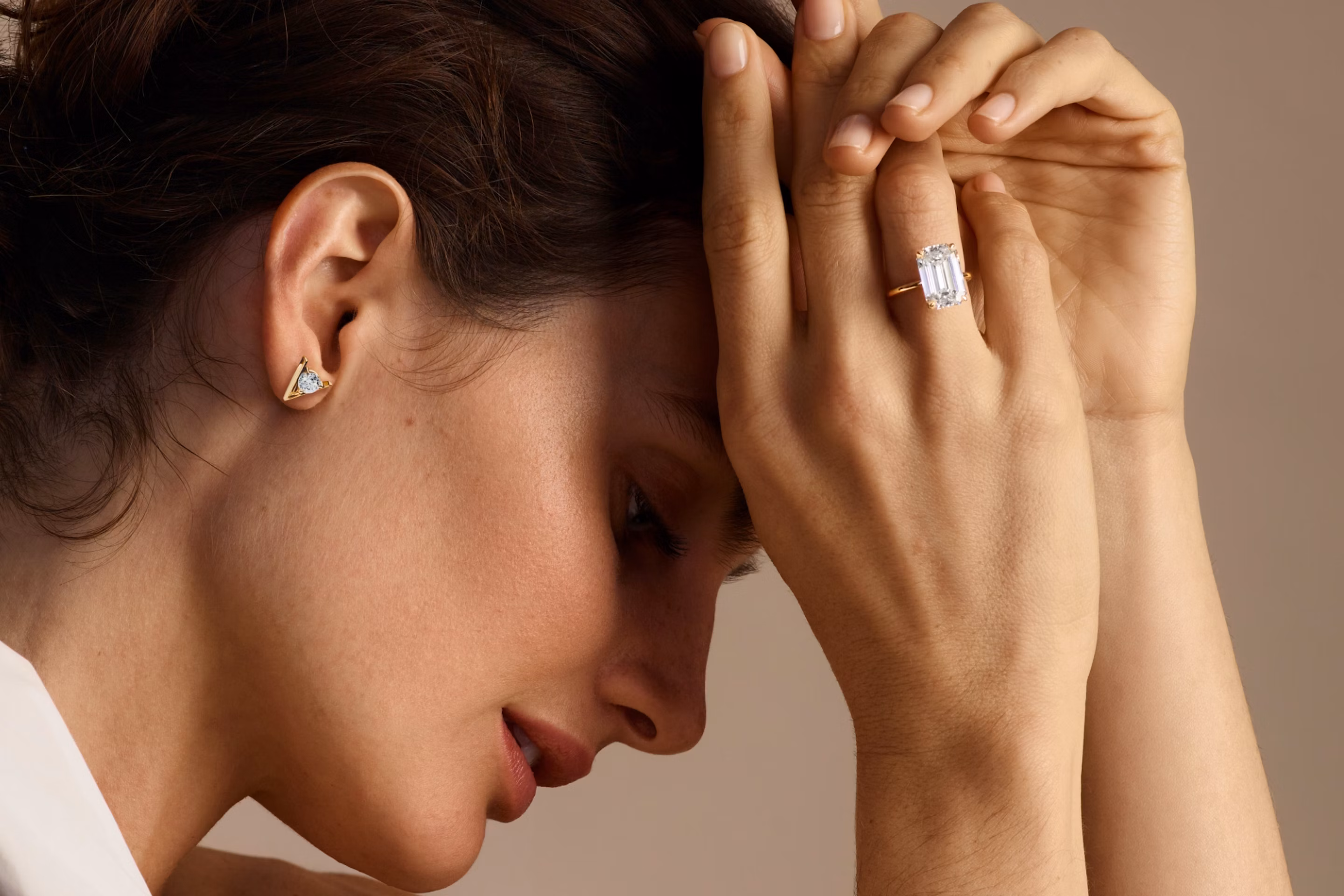 profile veiw of woman holding hands in front of head with a emerald cut engagement ring and wearing v studs earrings