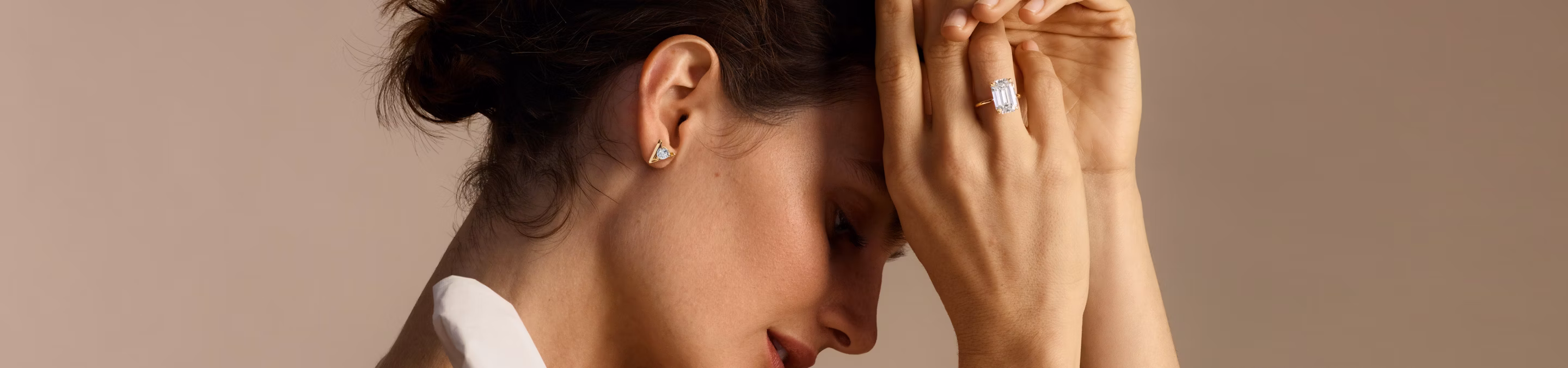 profile veiw of woman holding hands in front of head with a emerald cut engagement ring and wearing v studs earrings
