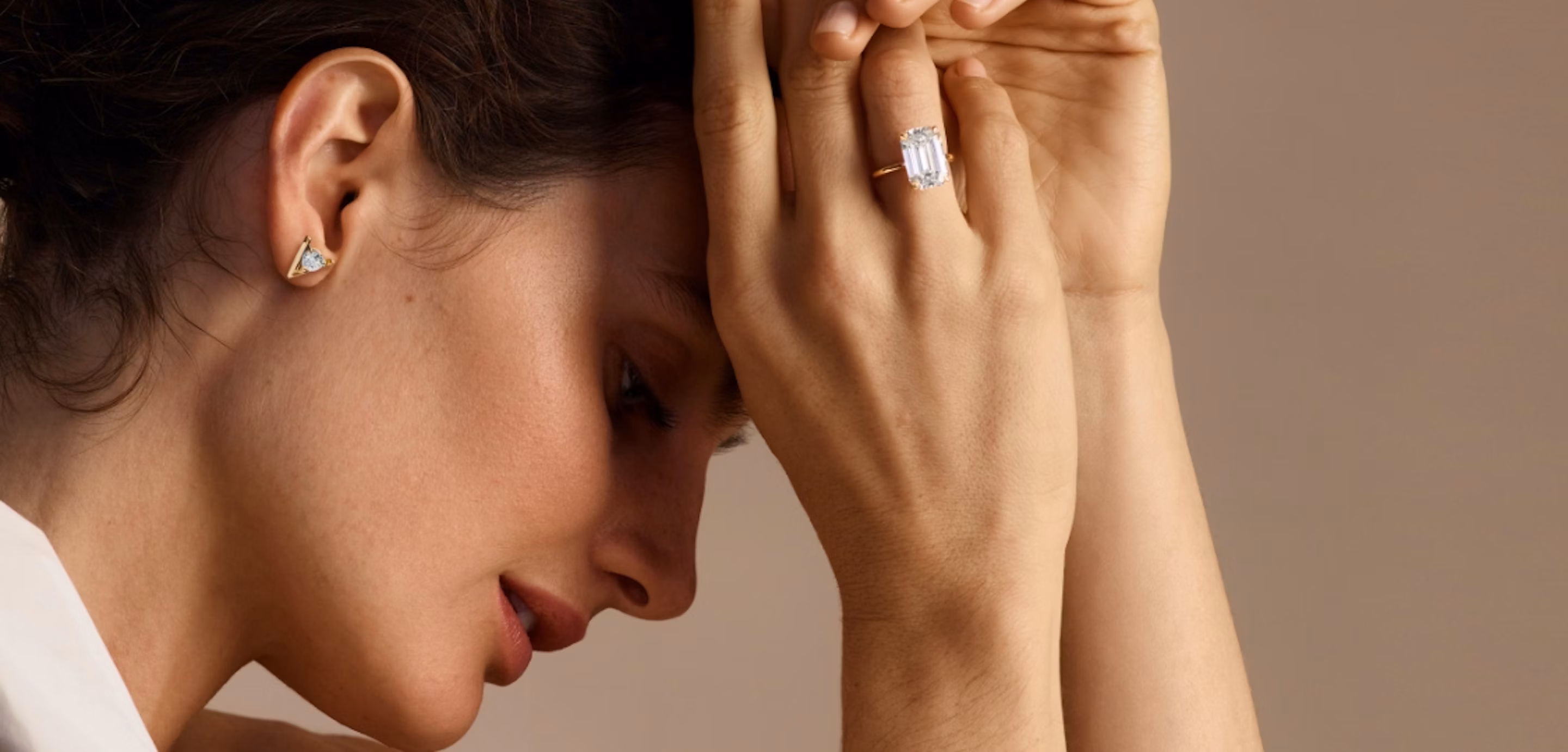 profile veiw of woman holding hands in front of head with a emerald cut engagement ring and wearing v studs earrings
