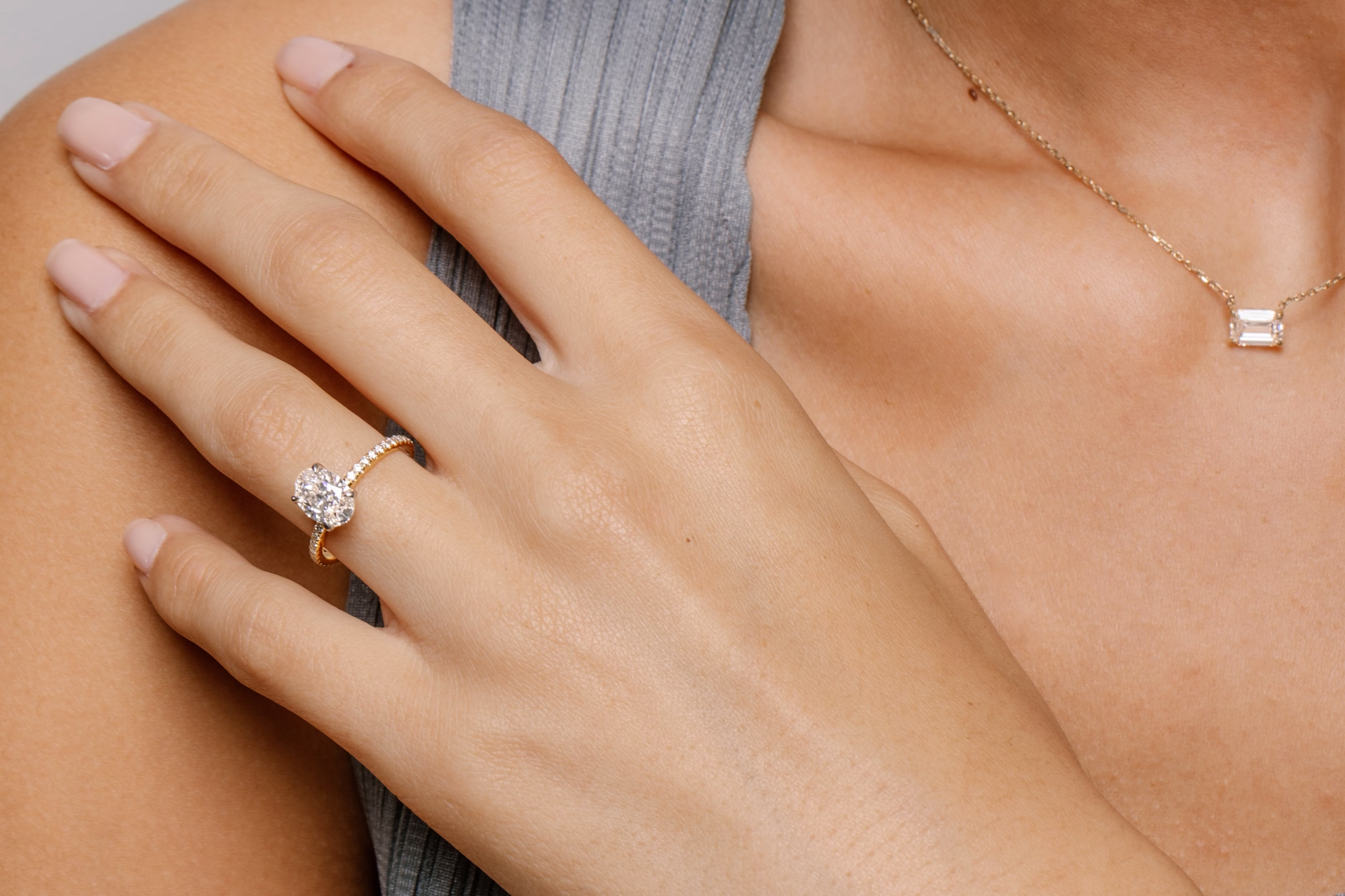 woman in athleisure top showing oval cut engagement ring and a pendant necklace
