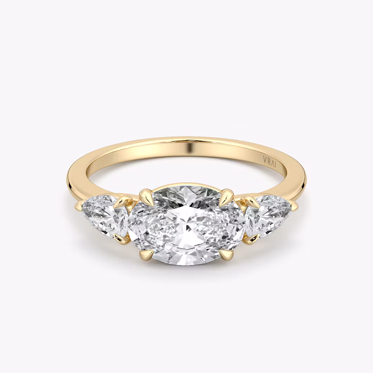 Oval-east-west-three-stone engagement ring with pear side stones on yellow gold band, front view on white background.