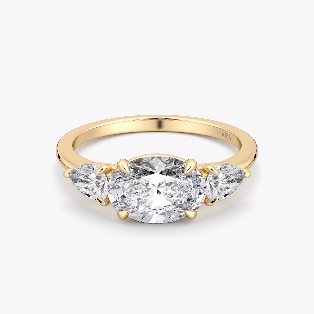 Oval-east-west-three-stone engagement ring with pear side stones on yellow gold band, front view on white background.