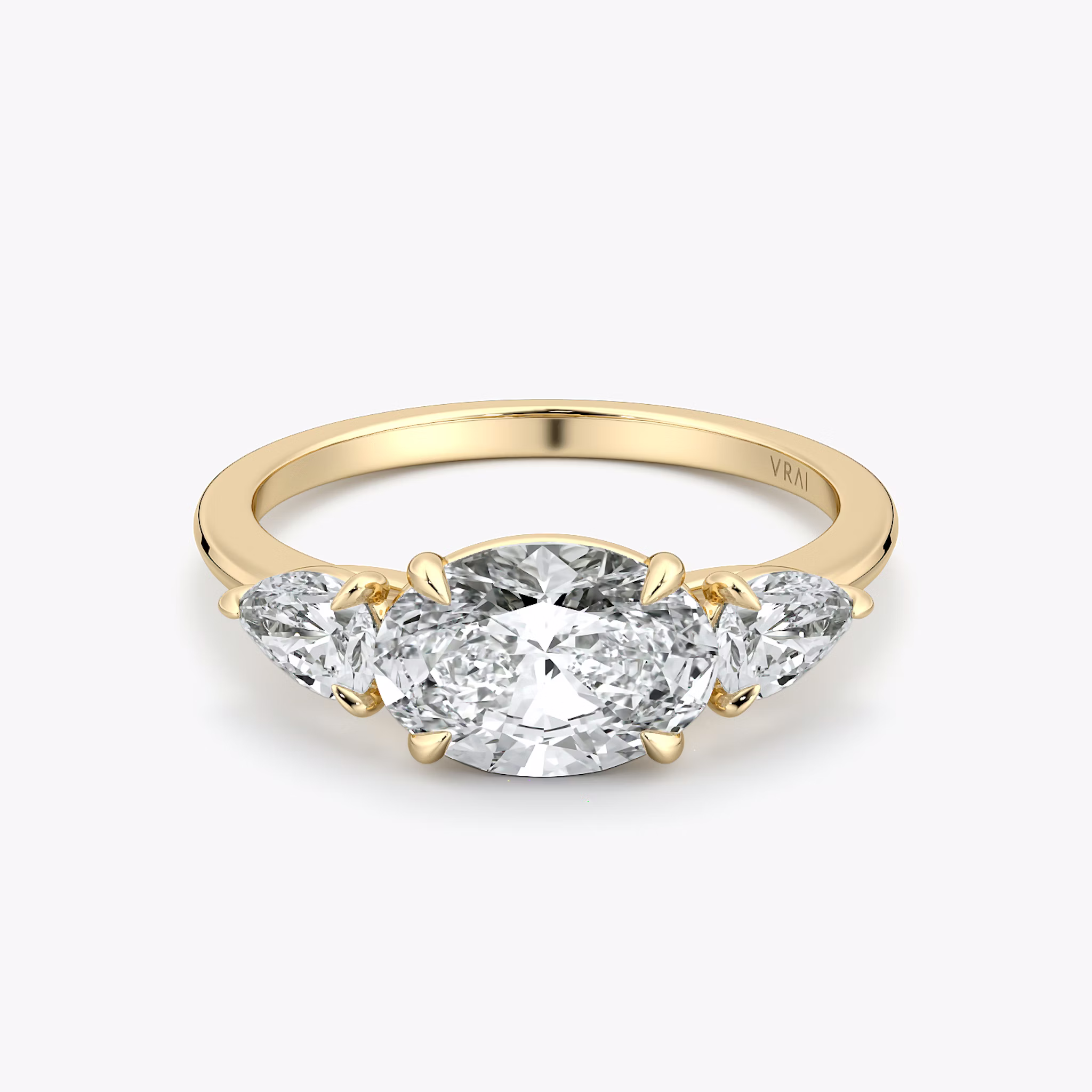 Oval-east-west-three-stone engagement ring with pear side stones on yellow gold band, front view on white background.