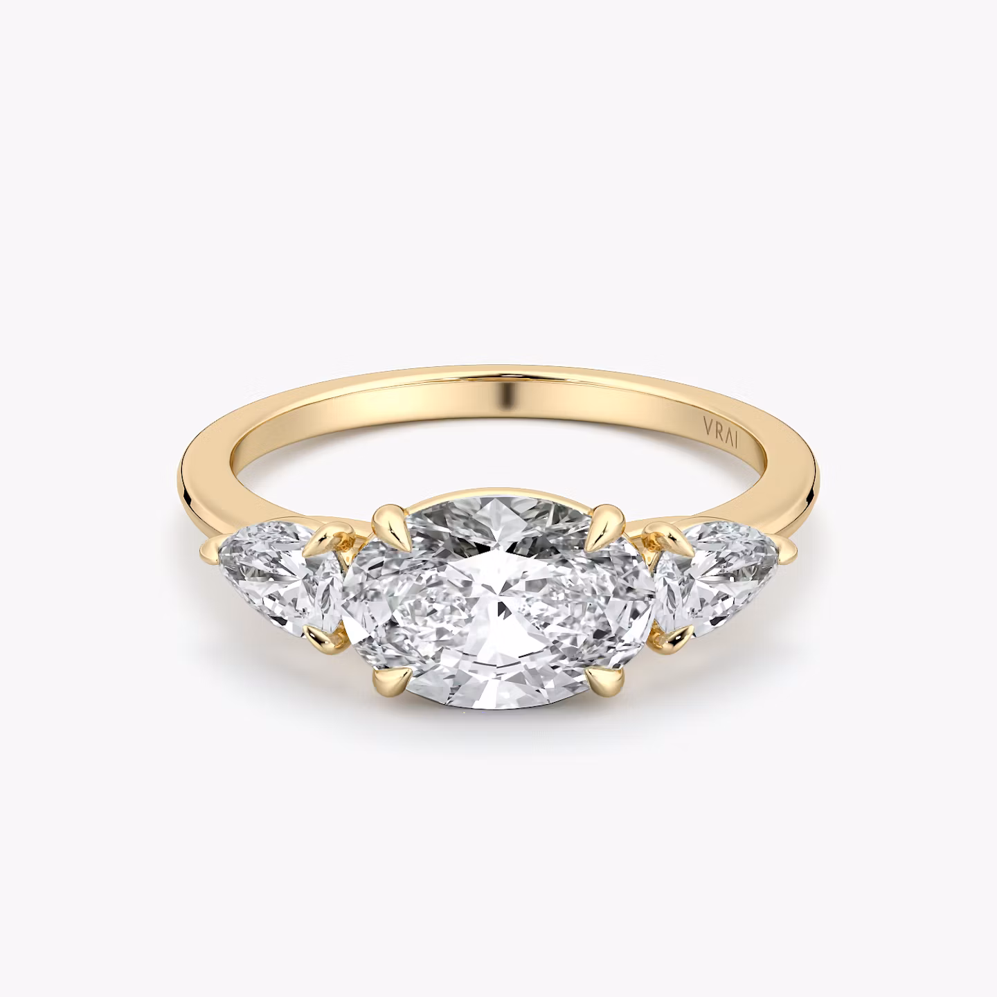 Oval-east-west-three-stone engagement ring with pear side stones on yellow gold band, front view on white background.