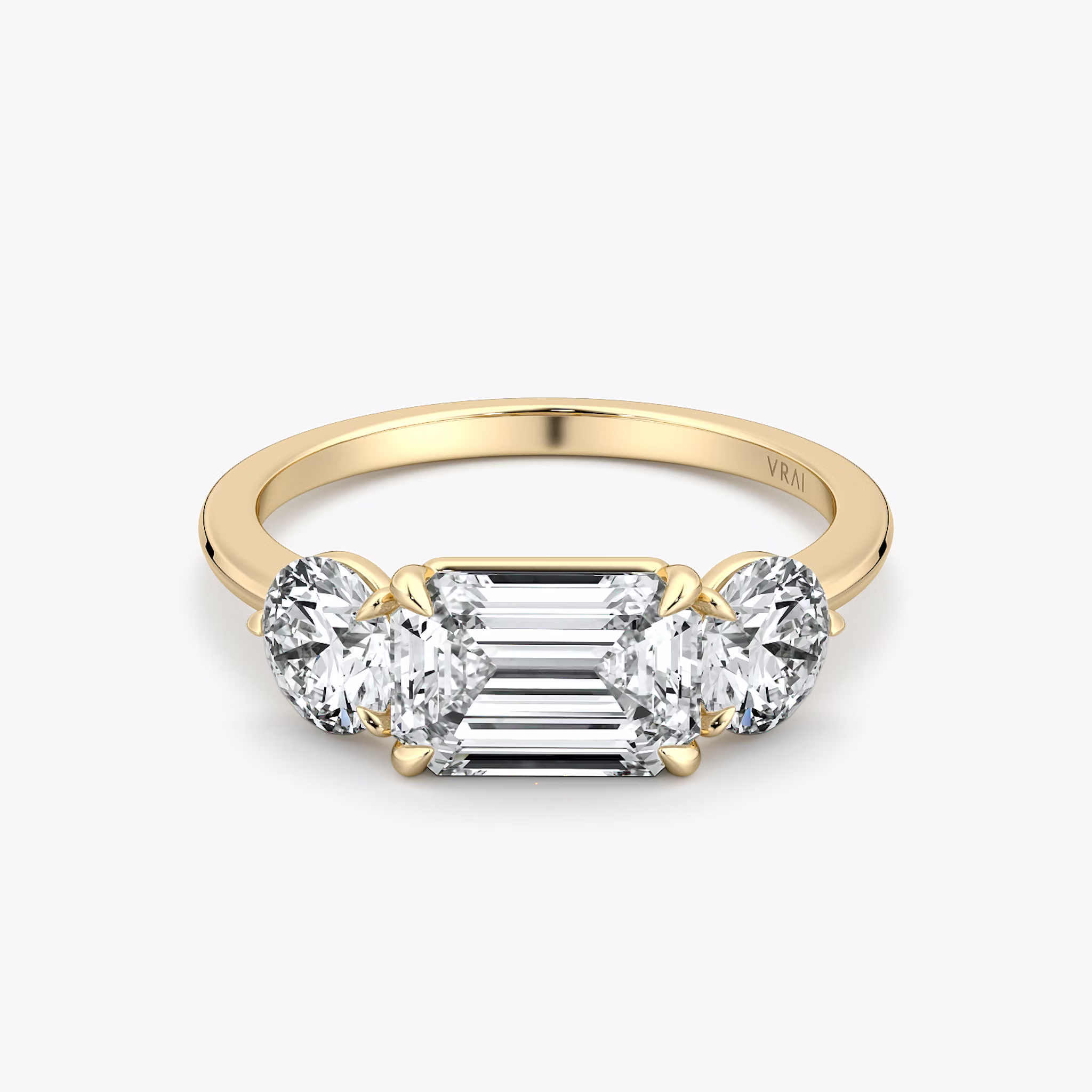 East-west three-stone engagement ring with emerald-cut center and round side diamonds on a yellow gold band, front view.