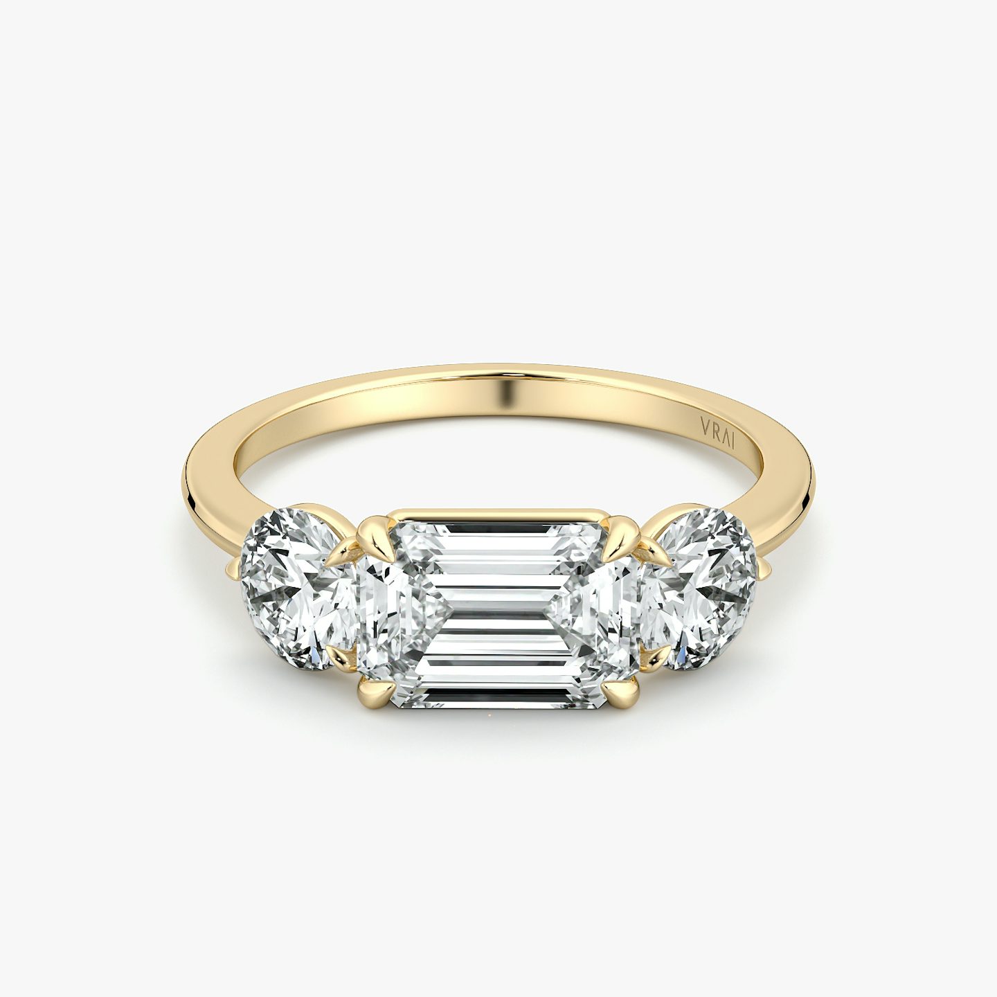 East-west three-stone engagement ring with emerald-cut center and round side diamonds on a yellow gold band, front view.