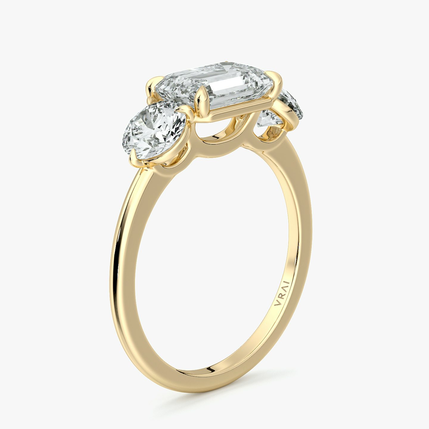 East-west three-stone engagement ring with emerald-cut center and round side diamonds on a yellow gold band, front view.