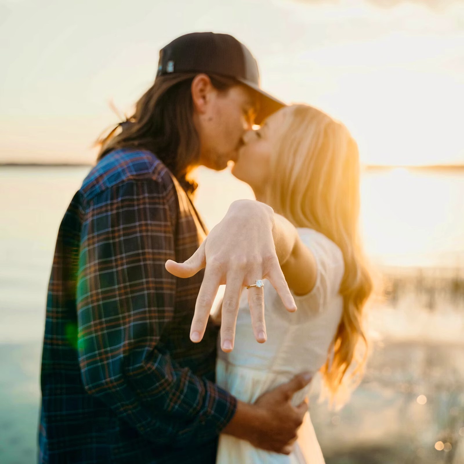 A couple is kissing while the woman holder her hand towards the camera, showing off her engagement ring.