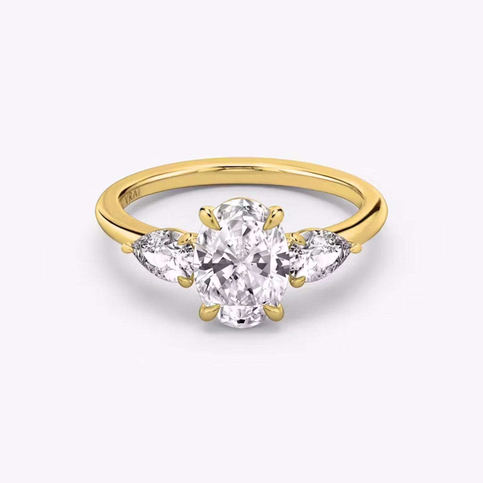 A close-up image of VRAI's Three Stone Oval Yellow Gold Engagement Ring, lying flat.