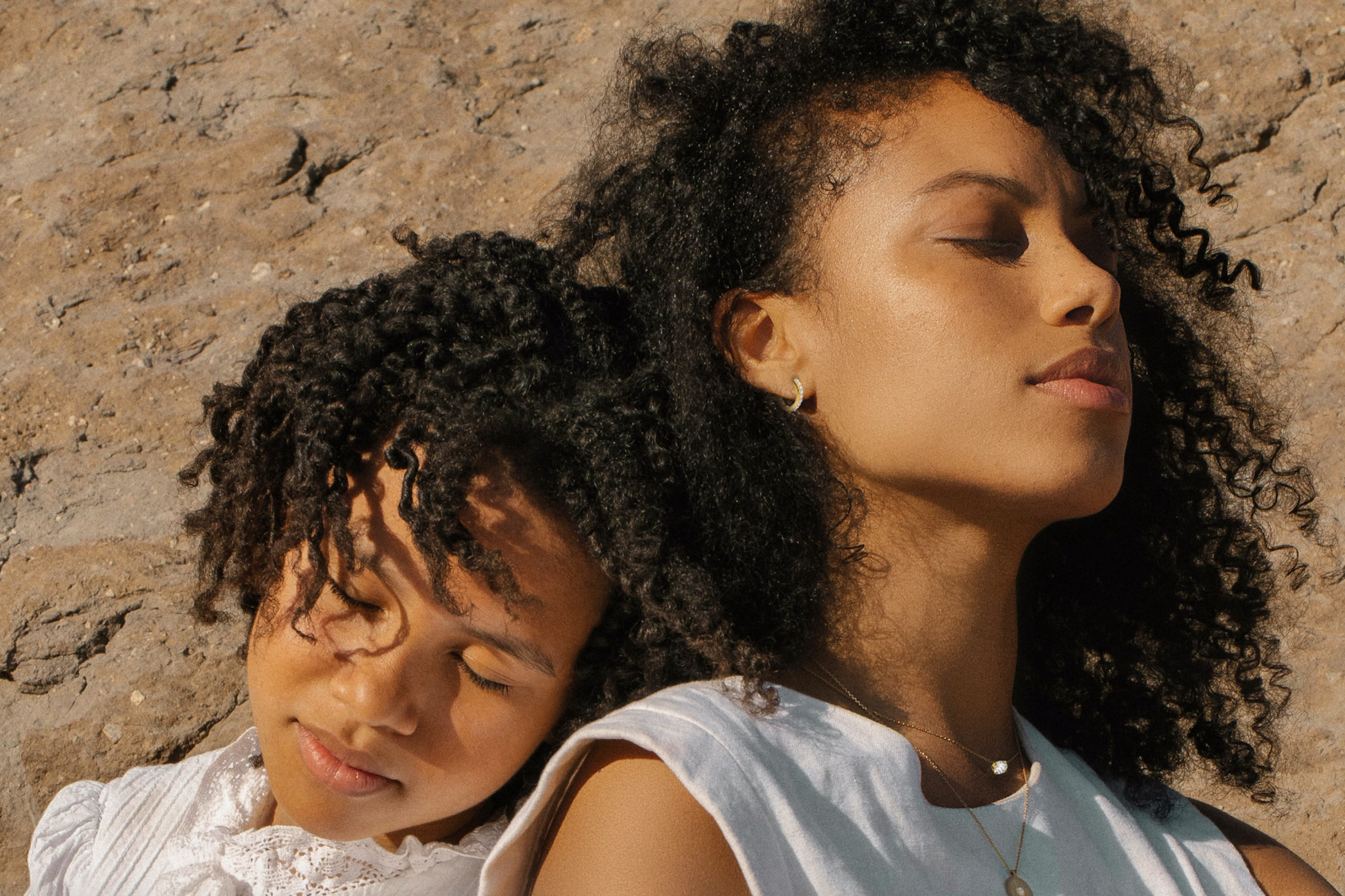 A mother and daughter are leaning against each other with their eyes closed.