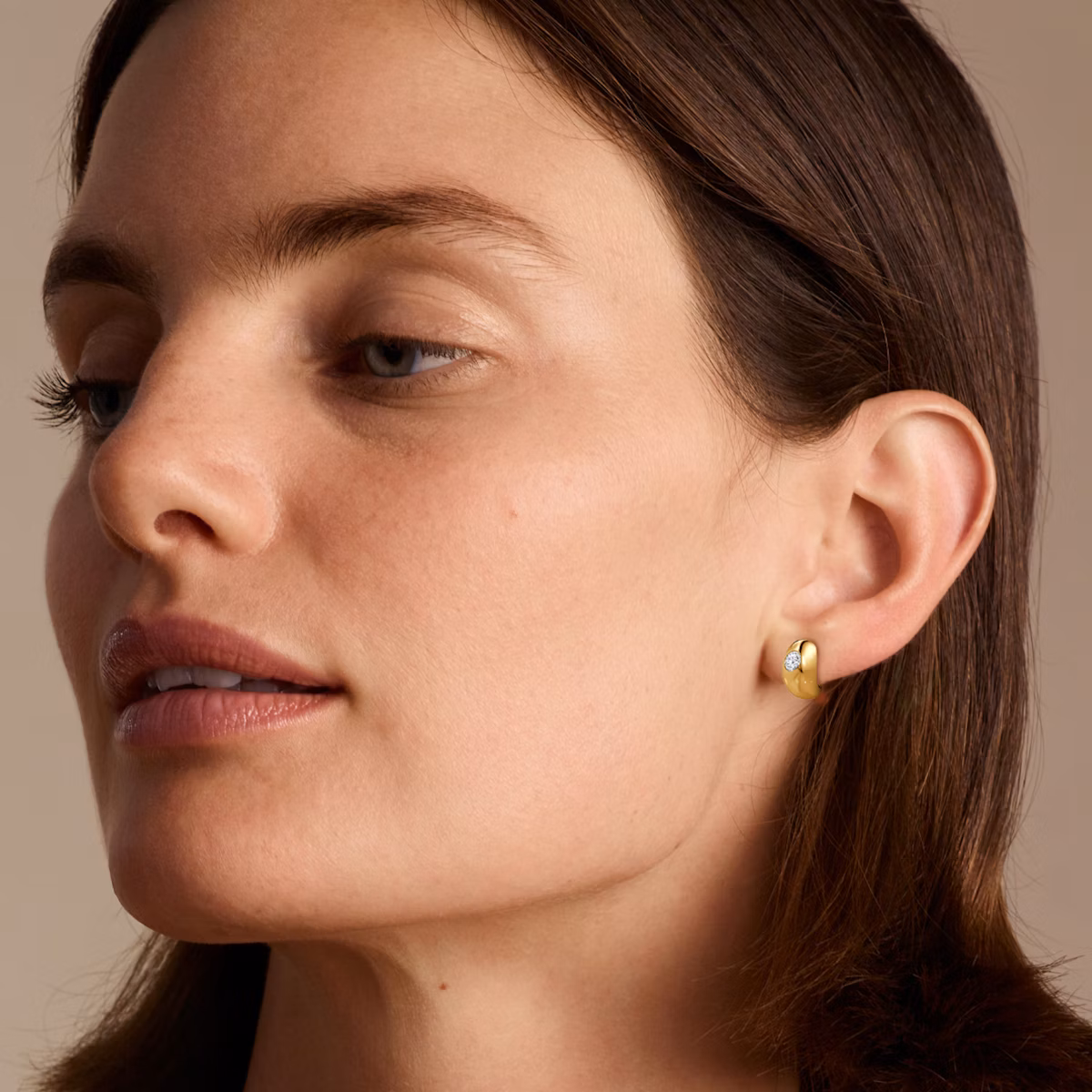 Model wearing yellow gold dome huggie hoop earring.