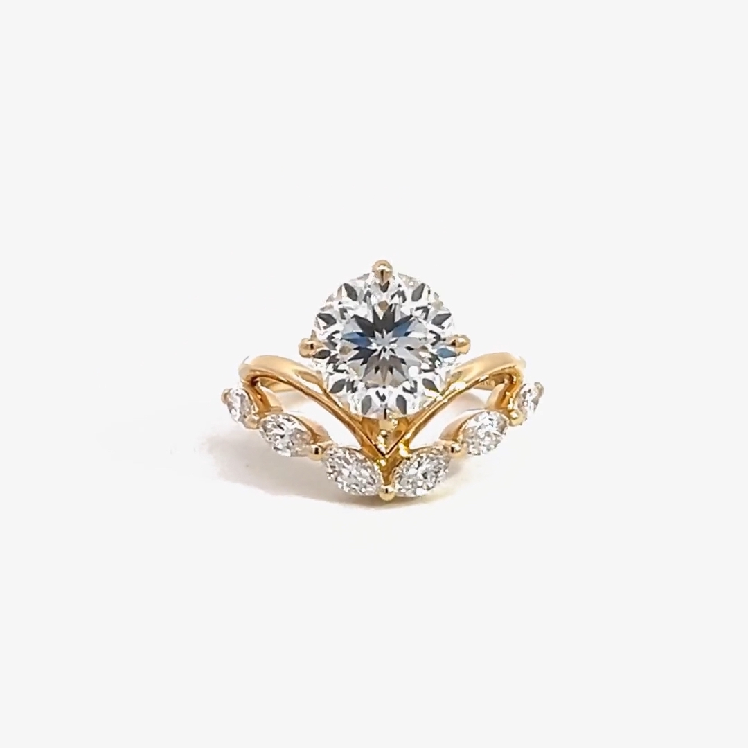 A gold VRAI created diamond, with a round center stone and smaller marquise cut diamonds below it.