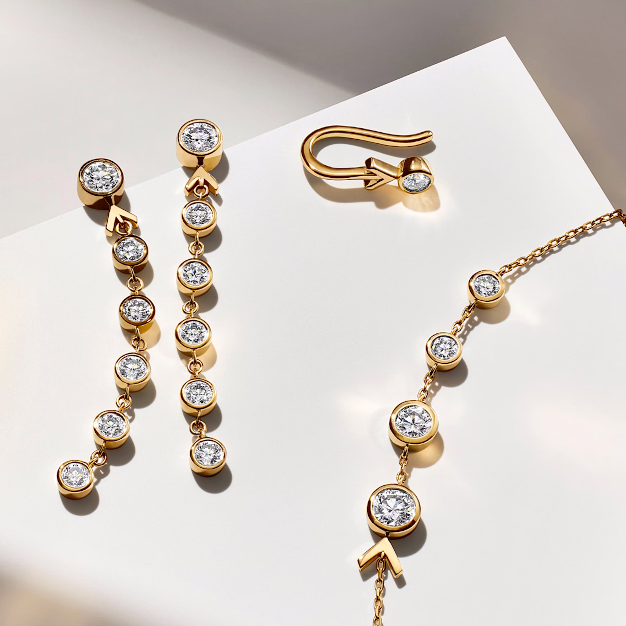 A yellow gold 0.10ct ear cuff, dangle earring and station bracelet on a table